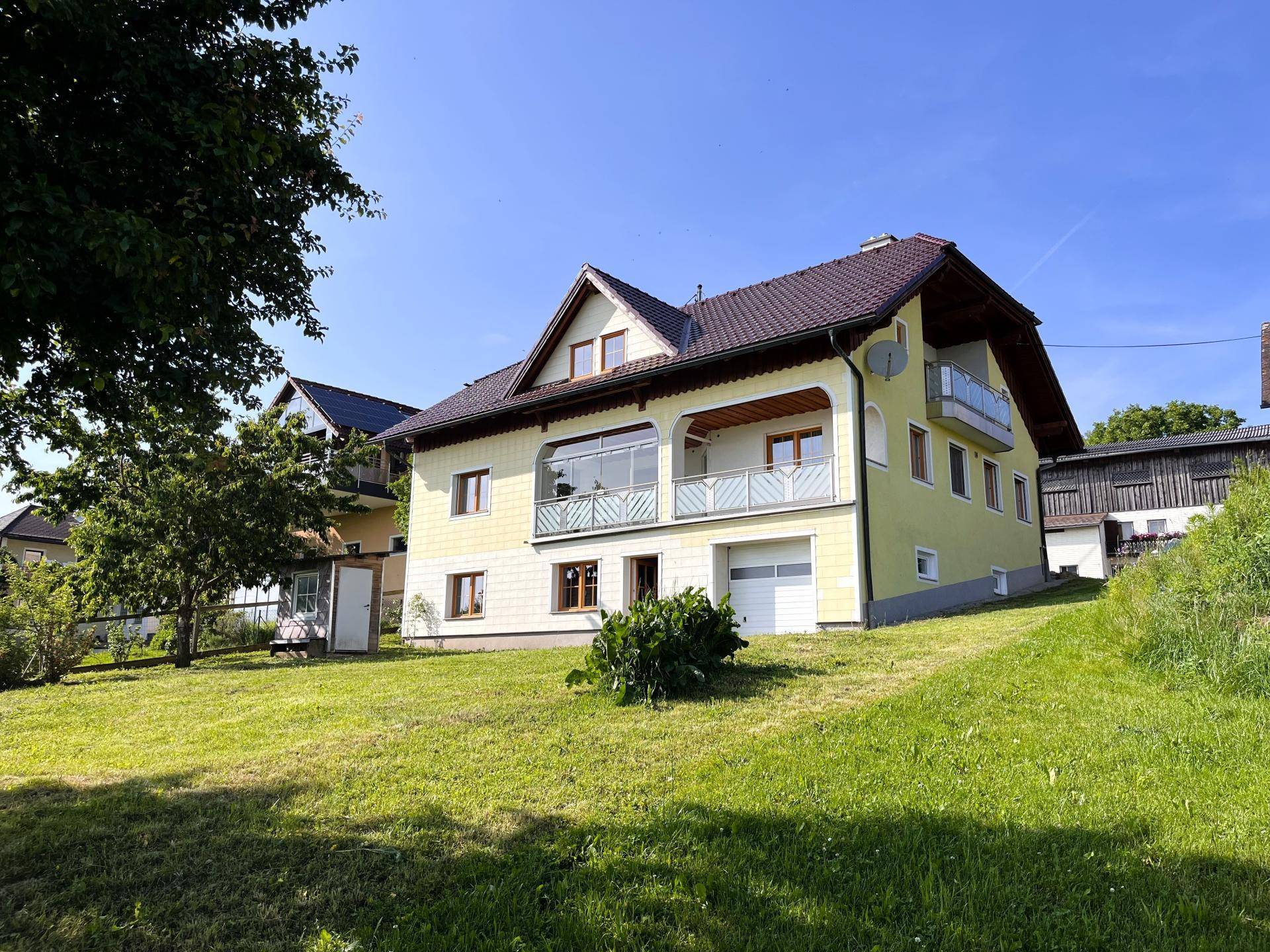 Rückansicht des Hauses mit großem Garten und Balkonen unter strahlendem Sonnenschein.