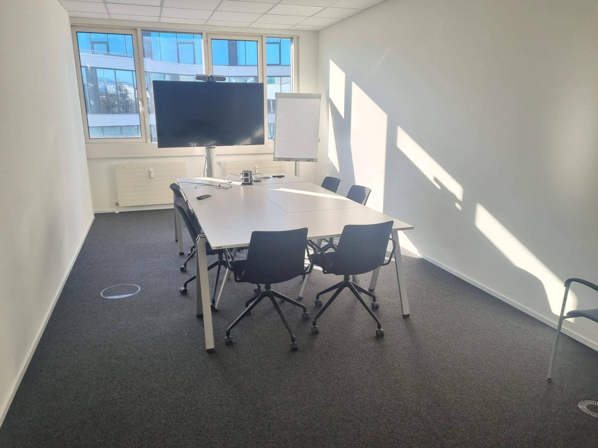 Heller Konferenzraum mit großem Tisch, Stühlen und einem Wandbildschirm, ideal für produktive Besprechungen.