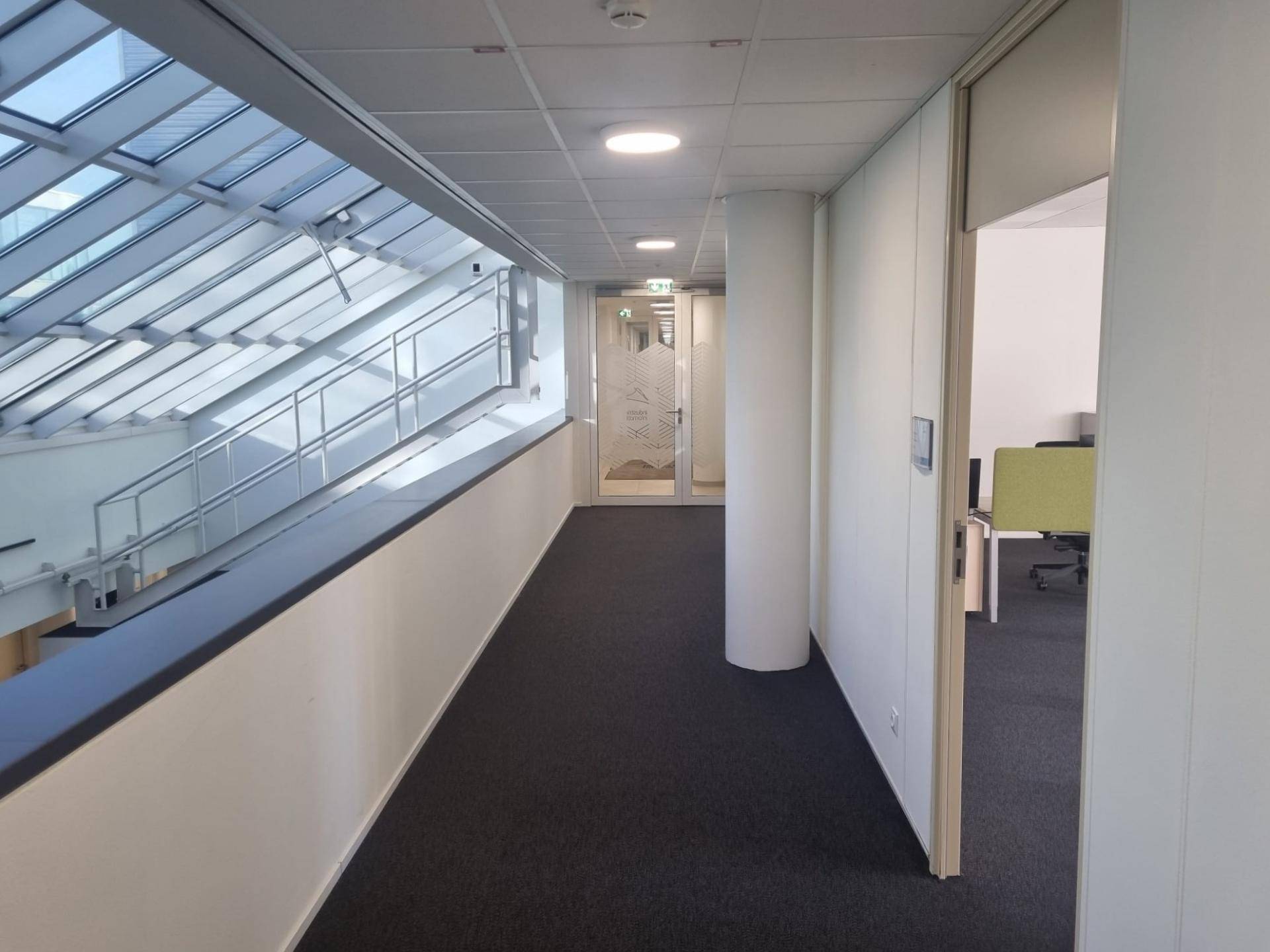 Heller Flur mit Teppichboden, Glasdach und Blick auf die untere Etage, modern und offen gestaltet.