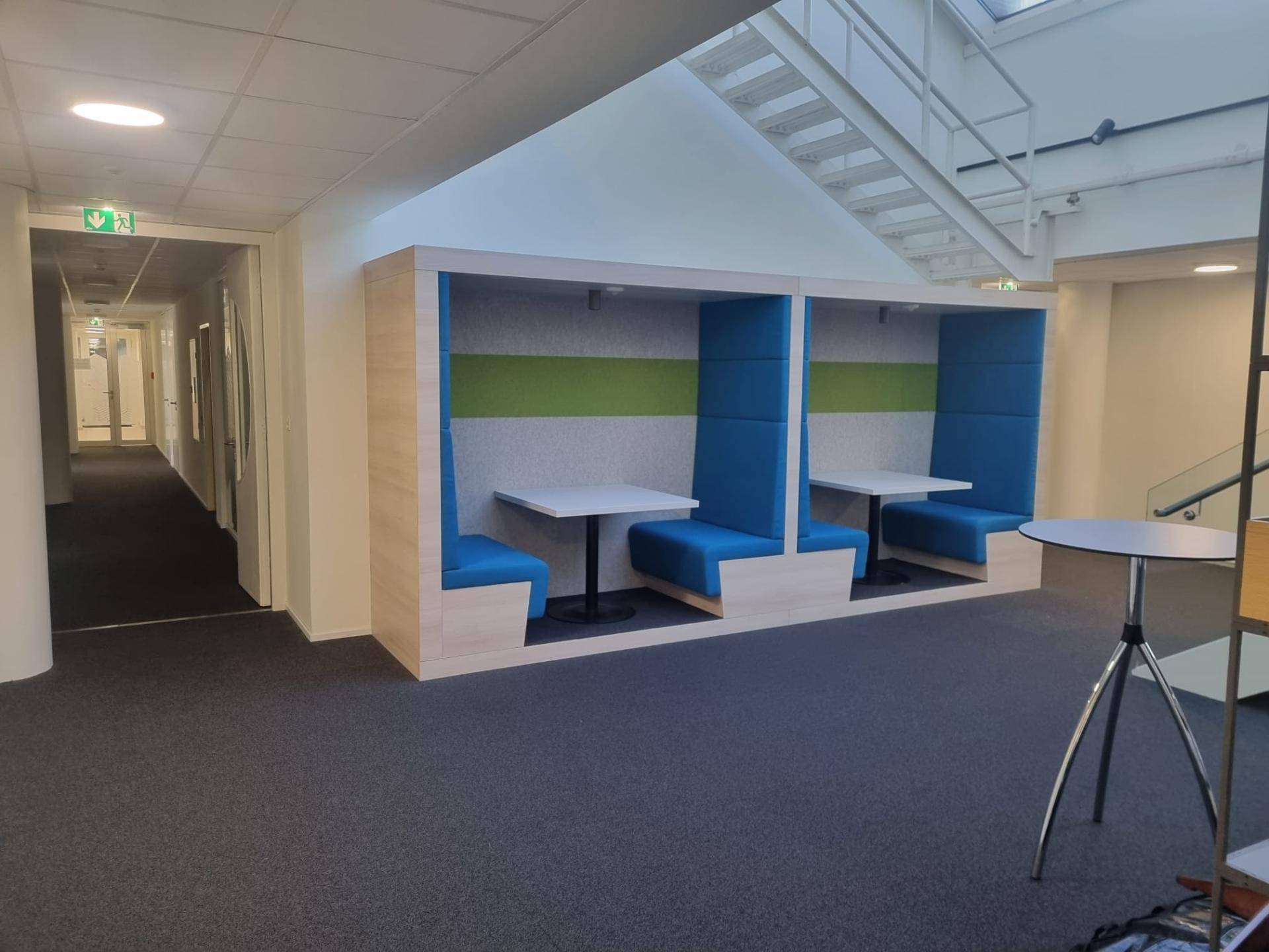 Gemütlicher Gemeinschaftsbereich mit blauen Sitzkabinen, kleinen Tischen und Teppichboden, ideal für Pausen.