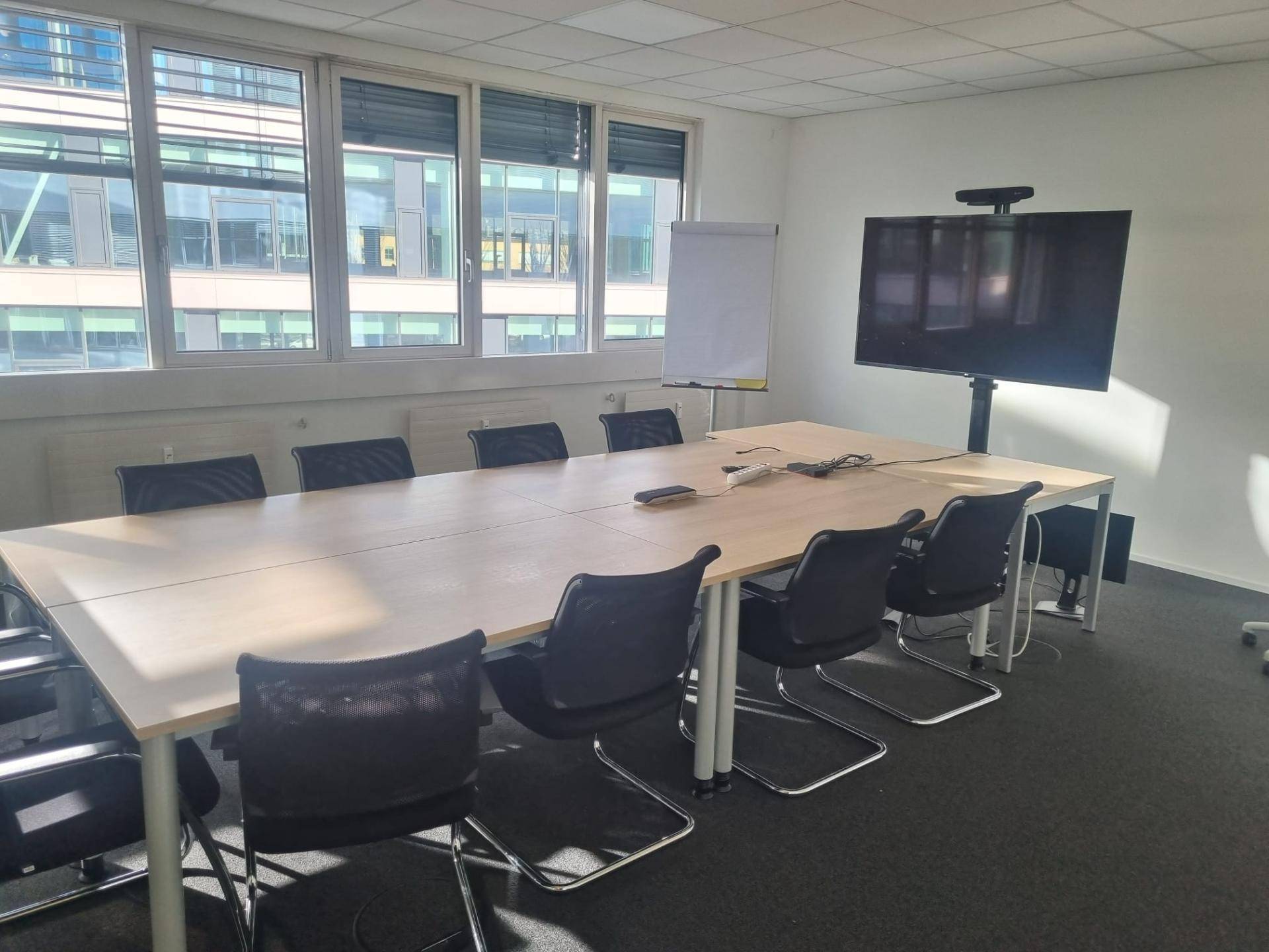 Geräumiger Konferenzraum mit langem Holztisch, vielen Stühlen und einem großen Bildschirm für Präsentationen.