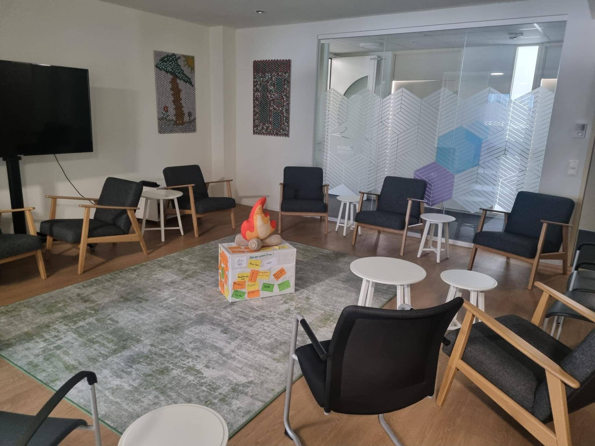 Entspannter Loungebereich mit bequemen Sesseln, Couchtischen und einem großen Bildschirm, modern eingerichtet.