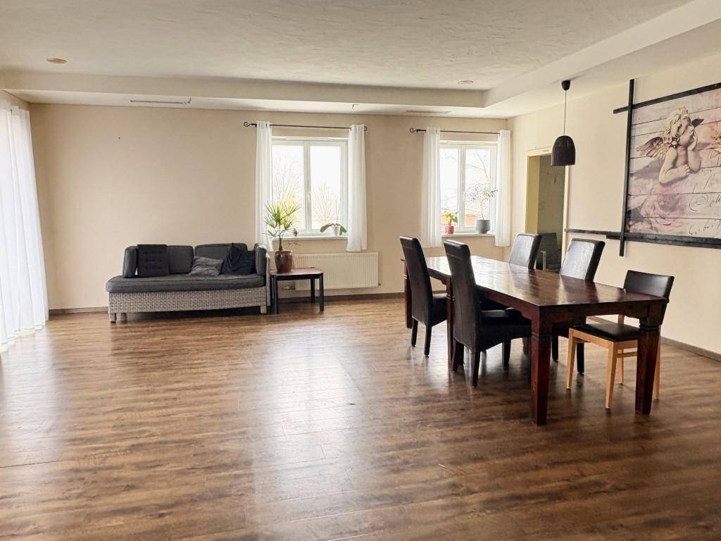 Geräumiger Wohn- und Essbereich mit Holzboden, einem großen Esstisch und einem Sofa.
