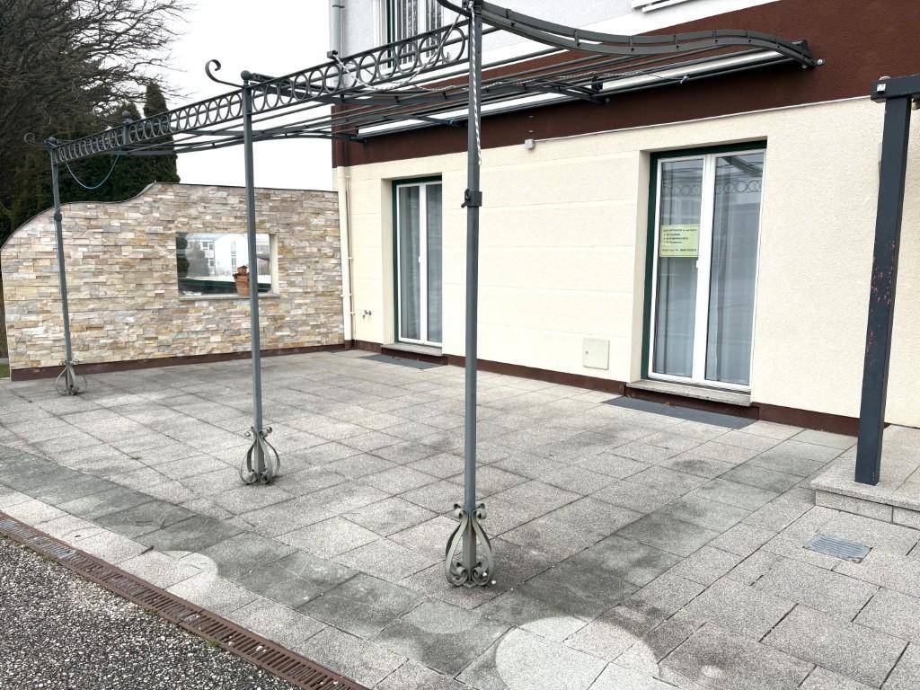 Große gepflasterte Terrasse mit einer dekorativen Metallüberdachung und Zugang zum Gebäude.