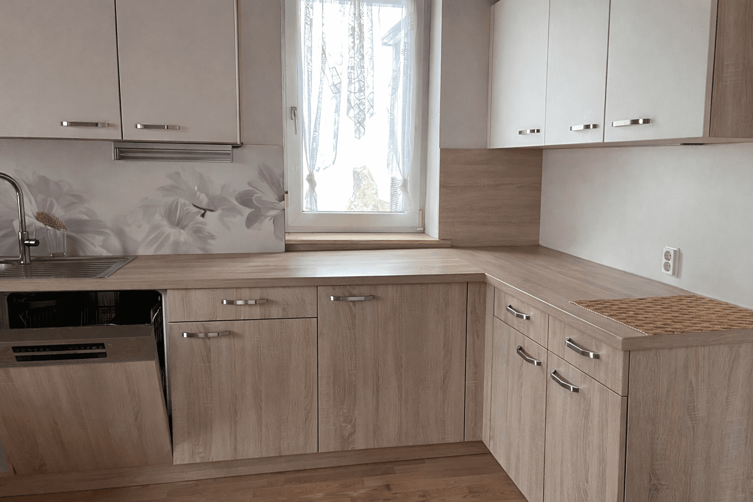 Einbauküche in Holzoptik mit Spülmaschine, Spüle und floraler Rückwandgestaltung.