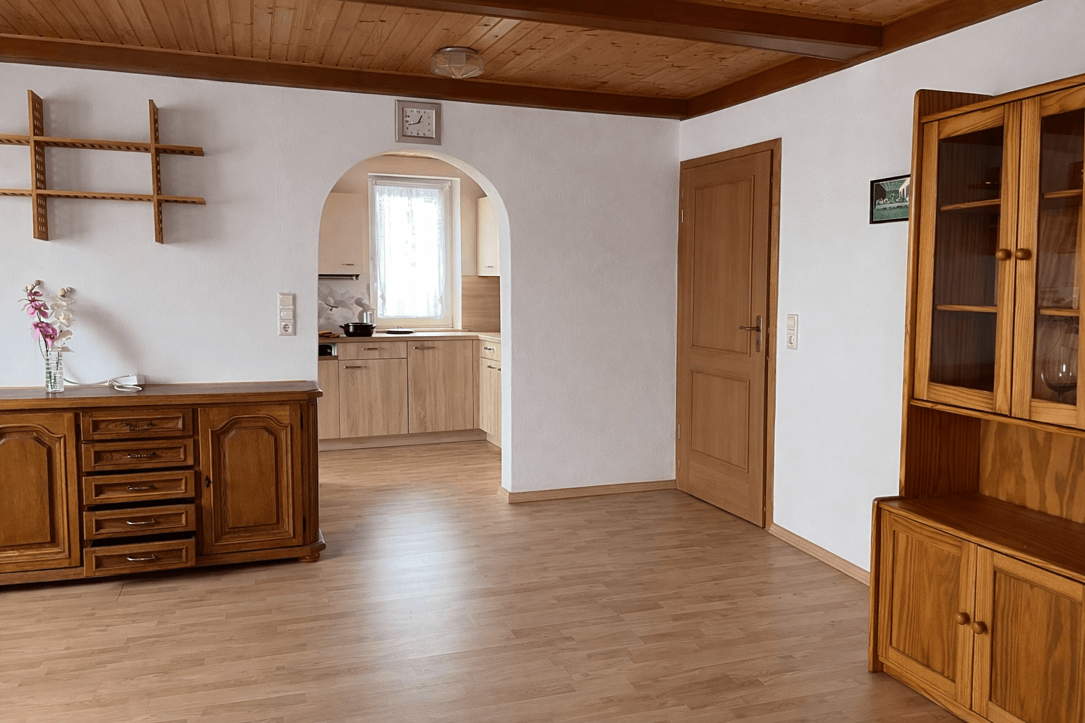 Wohnbereich mit Holzboden und Holzdecke, offenem Durchgang zur Küche und traditionellen Möbeln.