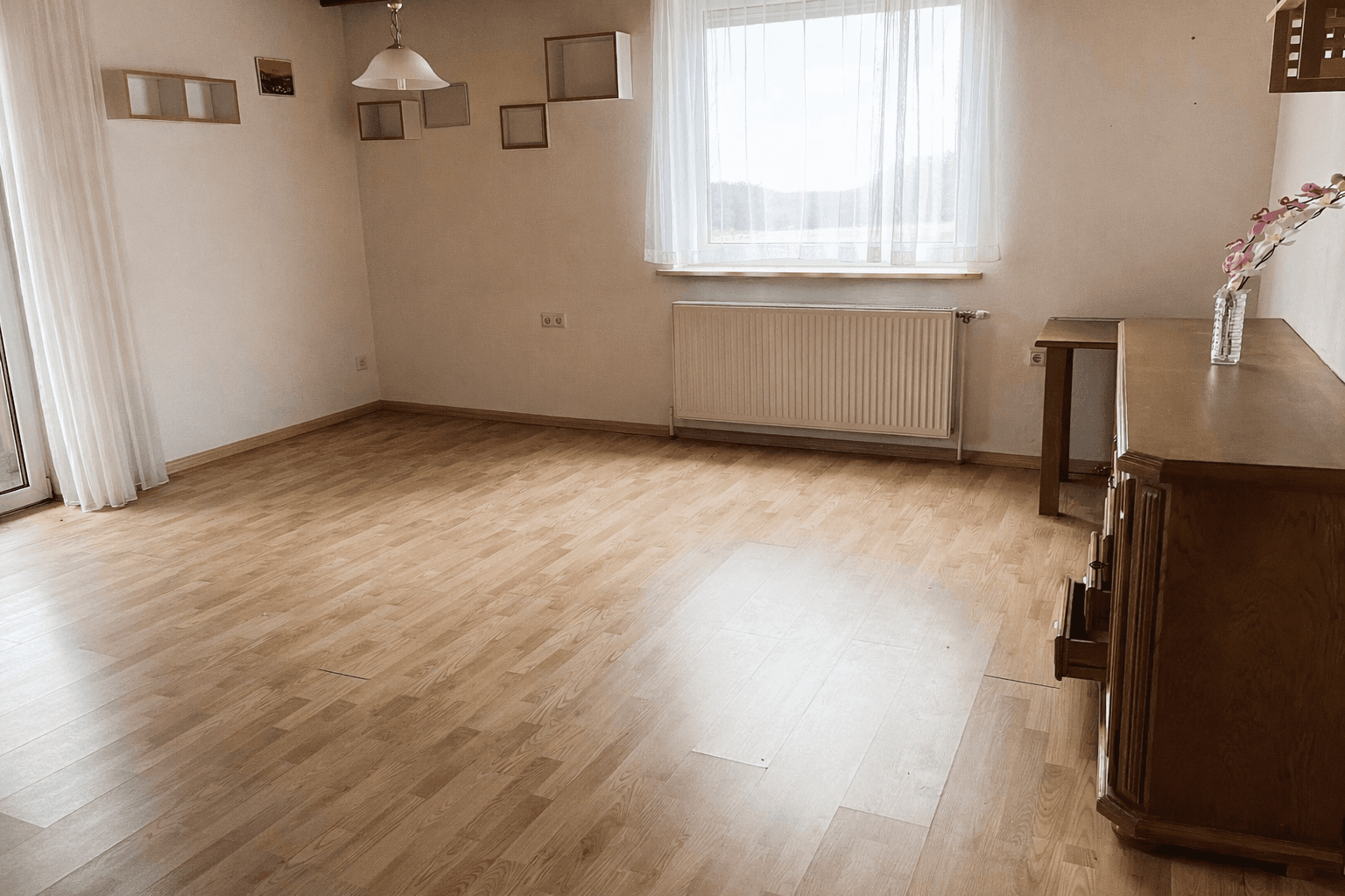 Heller Wohnraum mit Laminatboden, Holzdecke und großem Fenster für viel Tageslicht.