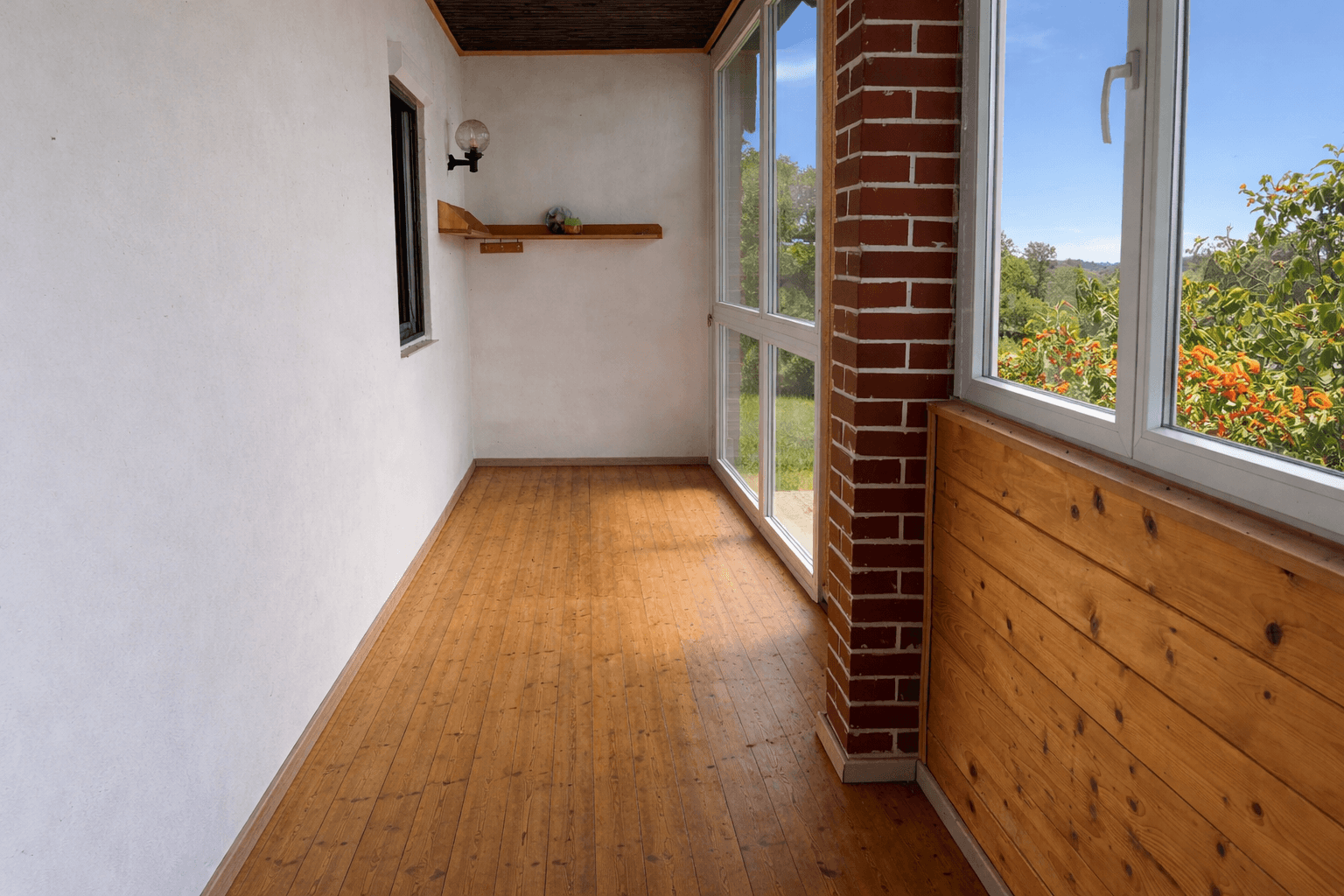 Heller Wintergarten mit Holzfußboden und großen Fenstern mit Blick ins Grüne.