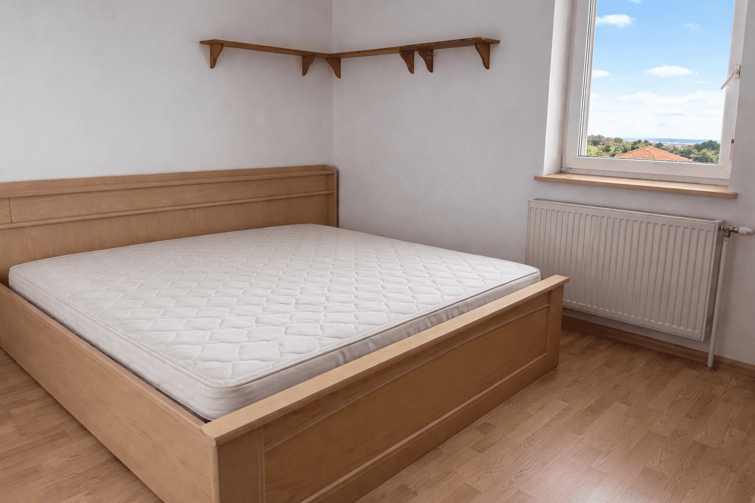 Schlafzimmer mit Holzbett, Laminatboden und Fenster mit Ausblick.