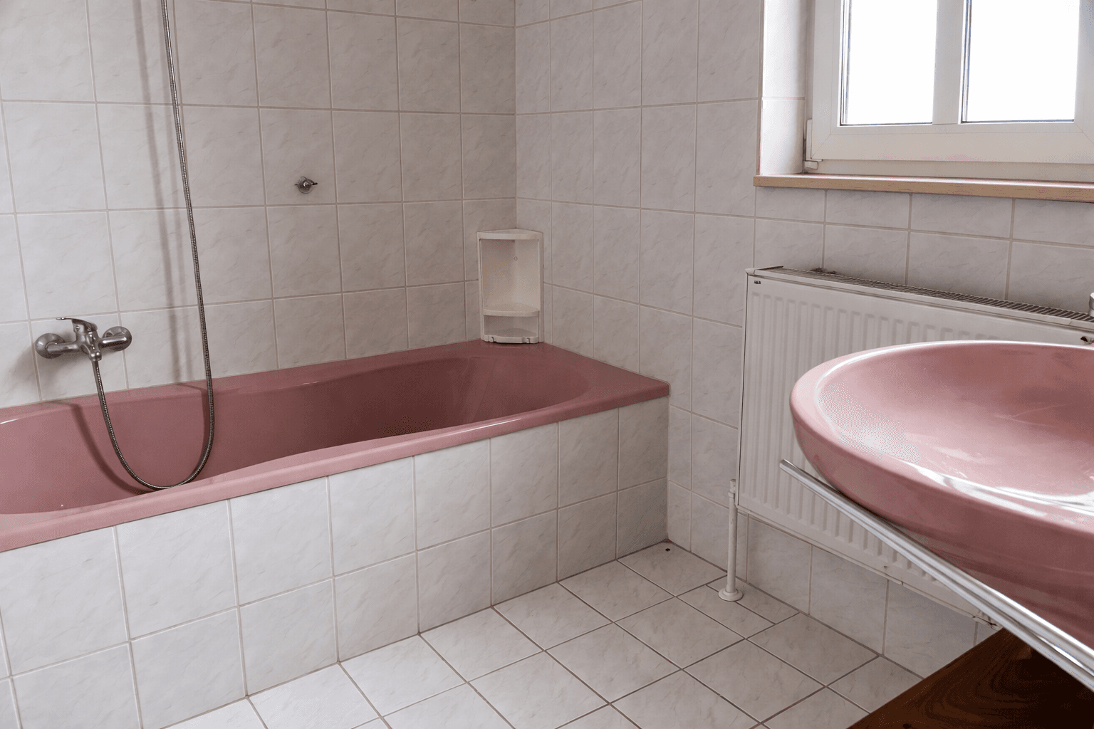 Badezimmer mit rosa Badewanne, Waschbecken und weißen Fliesen im 80er-Jahre-Stil.