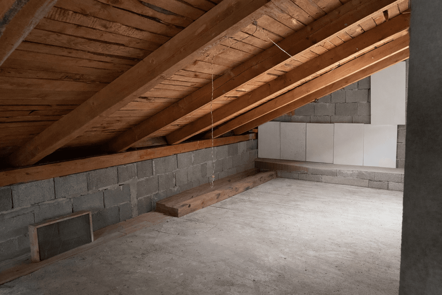 Dachboden mit sichtbaren Holzbalken und Betonwänden, bereit für Ausbau.