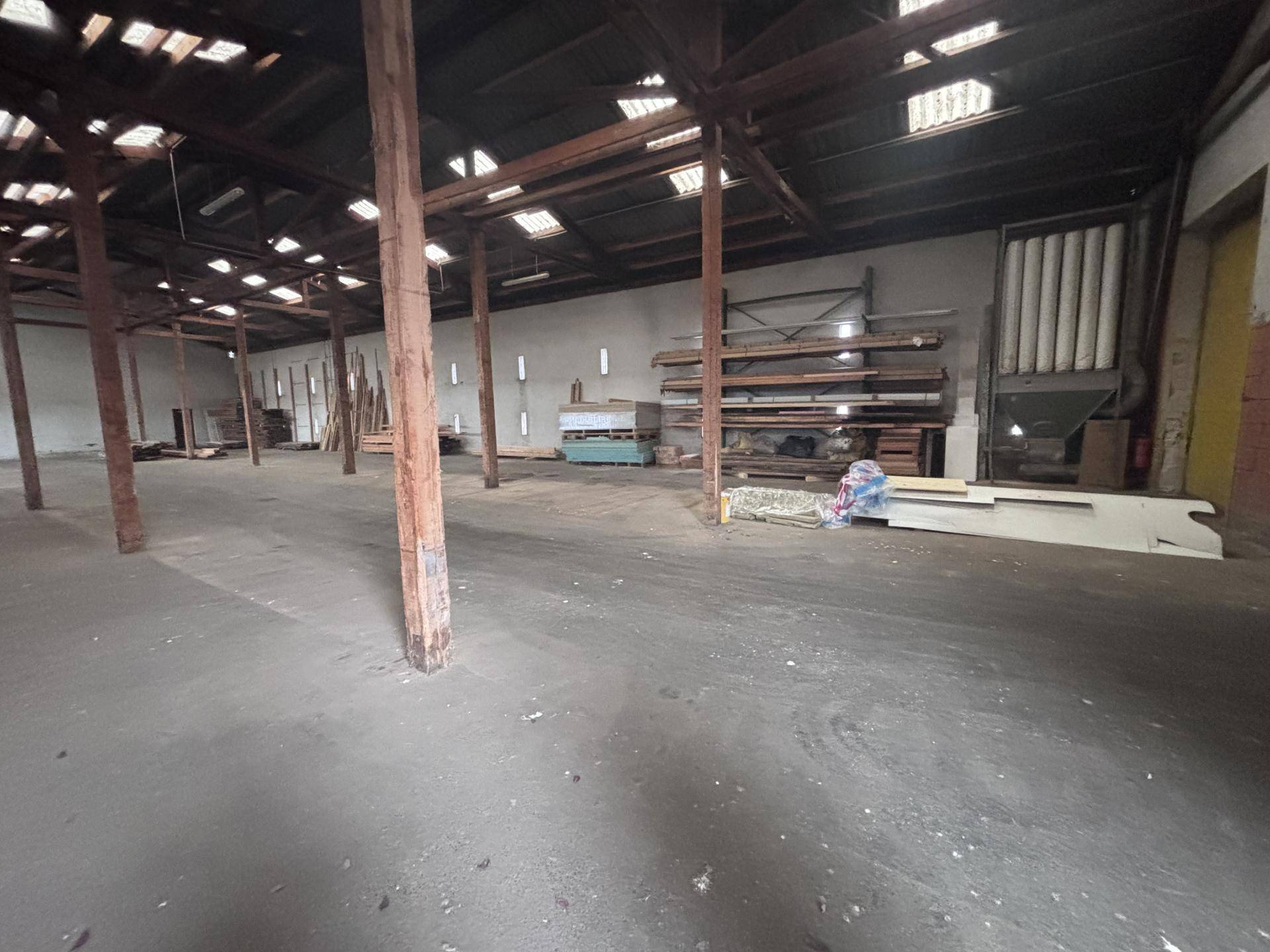Große leere Lagerhalle mit sichtbaren Holztragbalken und Betonboden, bereit zur Nutzung.