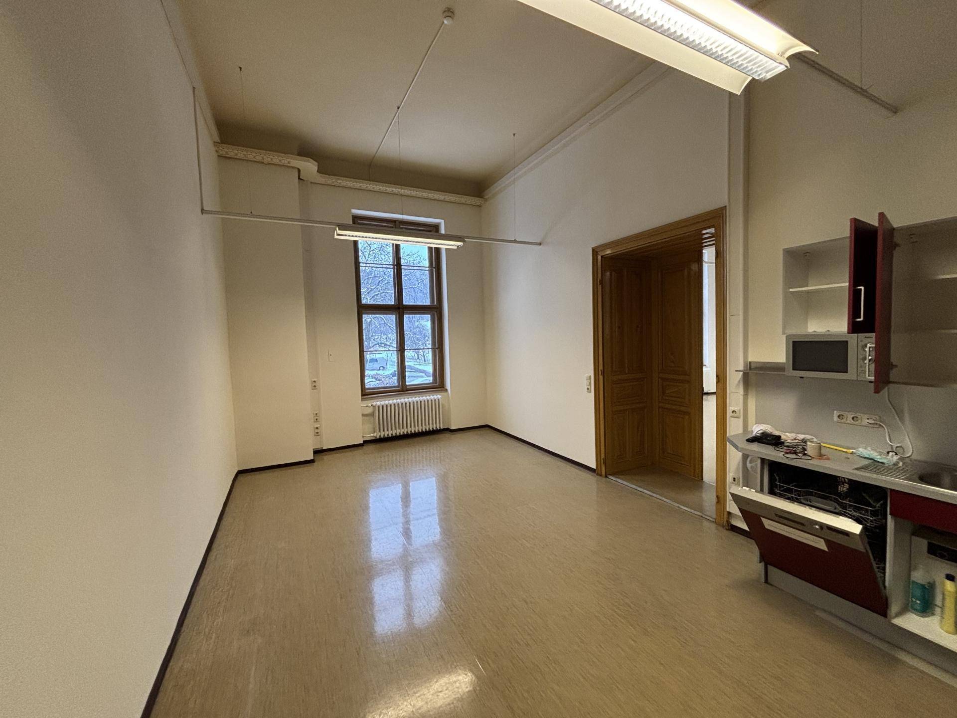 Heller Raum mit Fenster, kleiner Küchenzeile und Holztür, bietet funktionale Arbeitsumgebung.