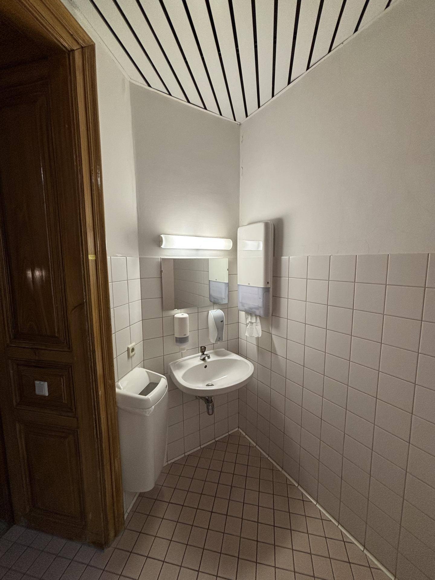 Kleiner Toilettenraum mit Waschbecken, Spiegel und Fliesen an Wänden und Boden.