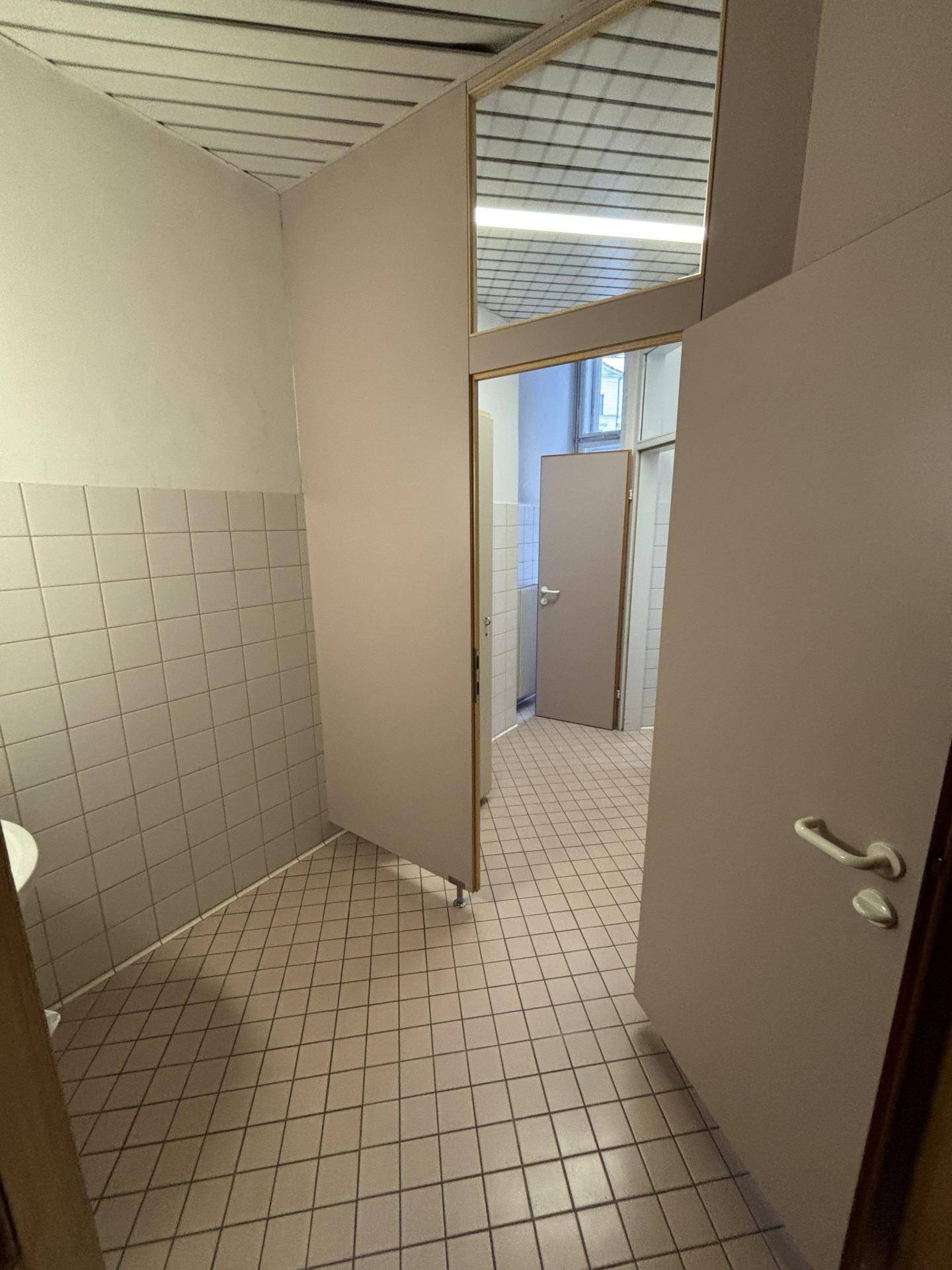 Gefliester Toilettenbereich mit mehreren Kabinen und Deckenplatten, funktional und sauber.