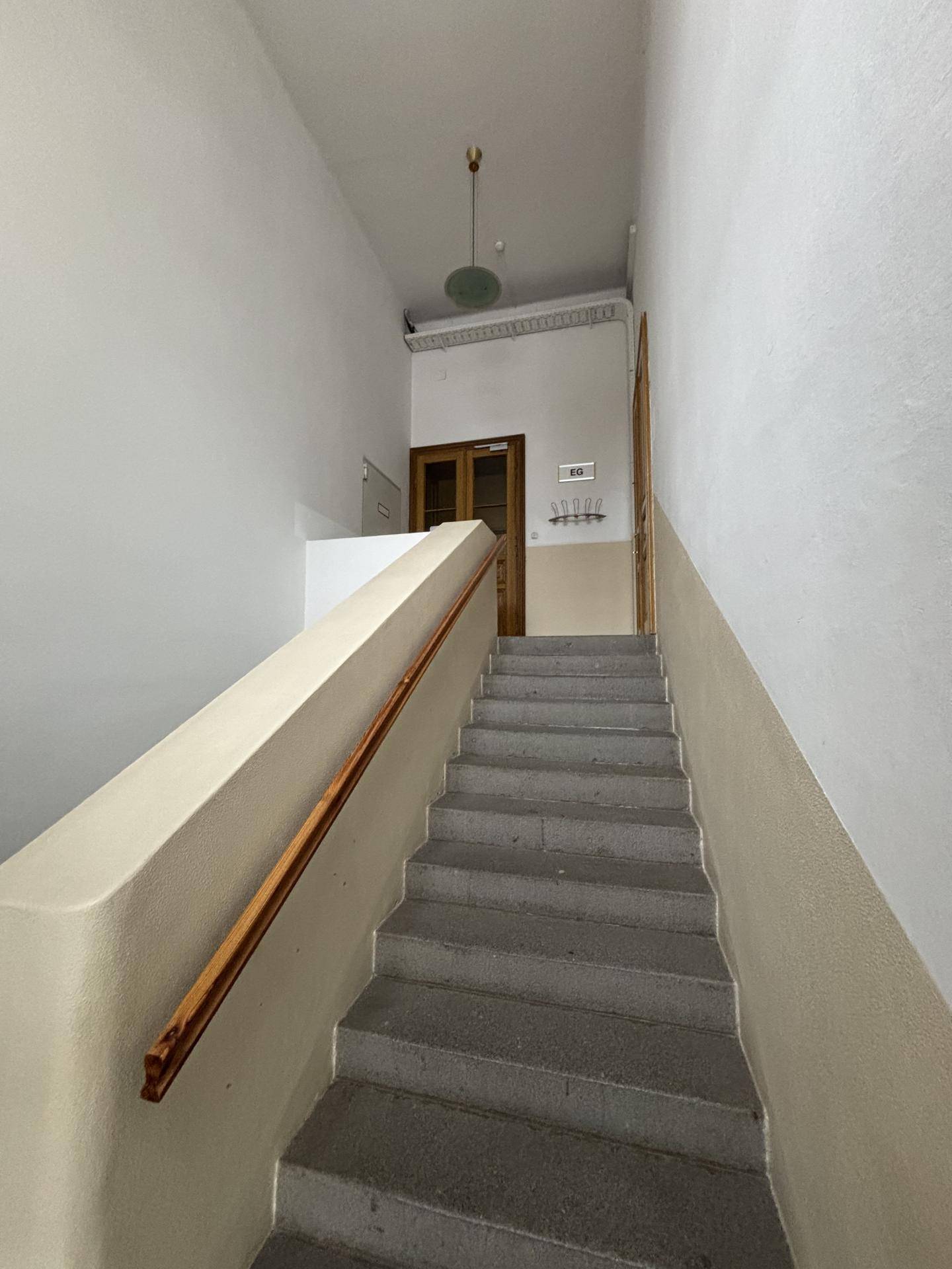 Treppenhaus mit Steinstufen, Holzgeländer und hohen Wänden, führt zu den oberen Etagen.