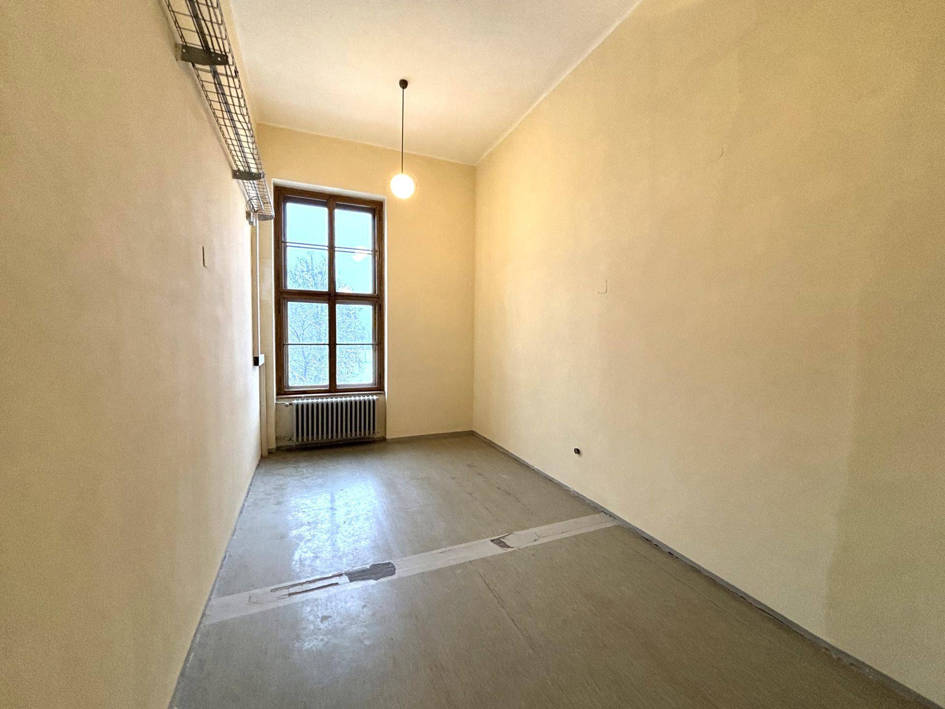 Leerer Raum mit einem Fenster, beigem Anstrich und sichtbaren Kabelkanälen an der Decke.