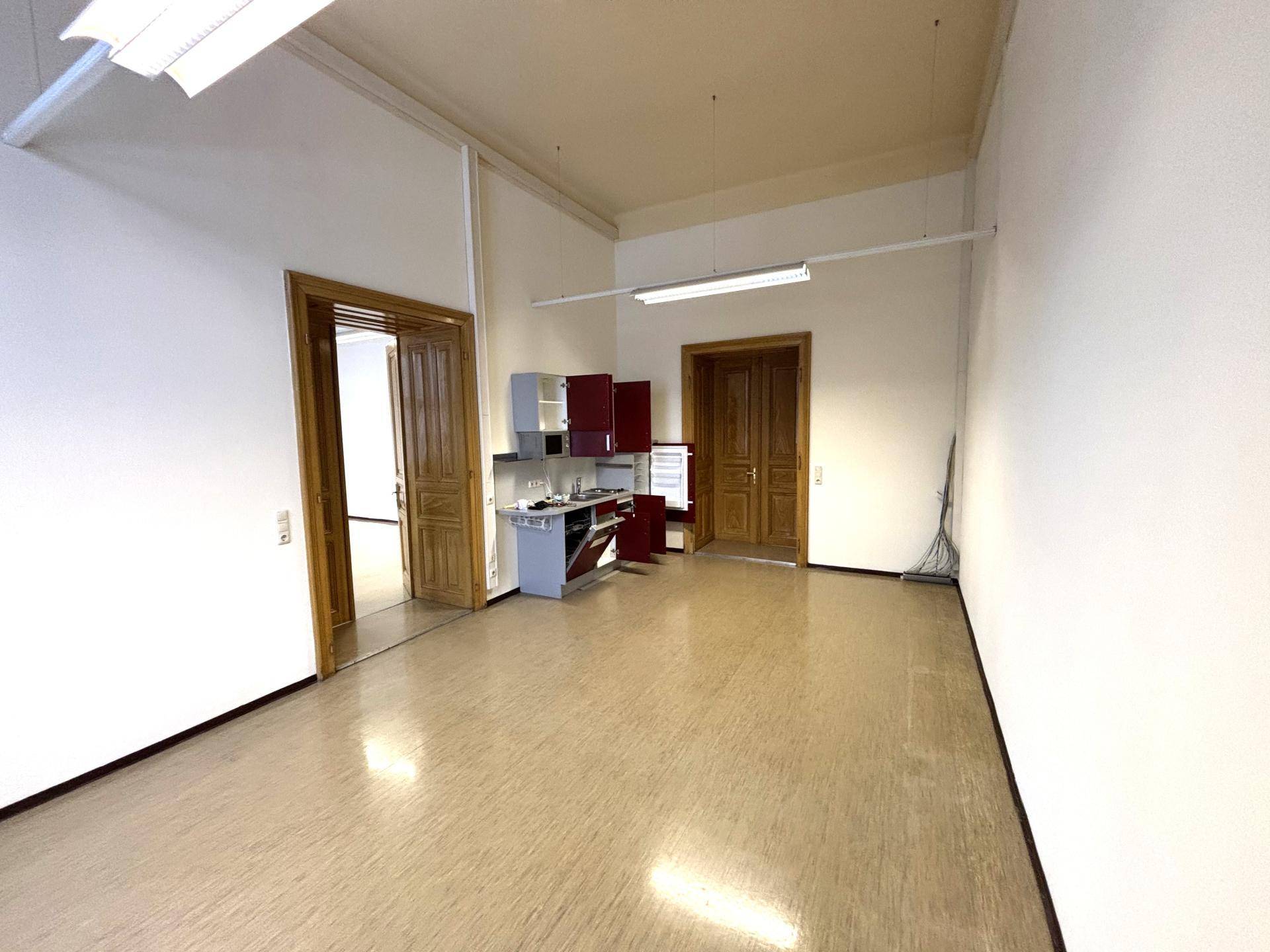 Geräumiger Raum mit einer kleinen Küchenzeile und Holztüren, ideal für Büro oder Gemeinschaftsbereich.