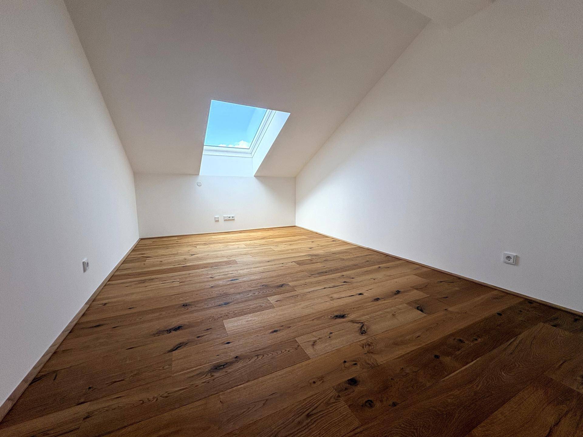 Geräumiges Dachzimmer mit Holzboden und einem hellen Dachfenster, perfekt für ein Kinder- oder Gästezimmer.