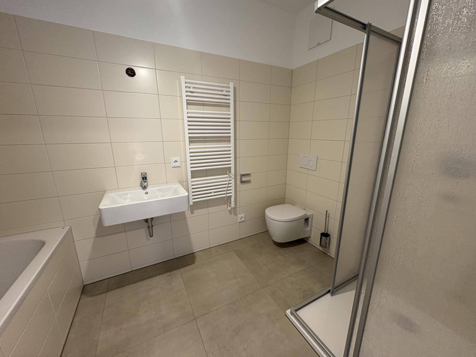 Modernes Badezimmer mit beigefarbenen Fliesen, Badewanne, Dusche und Wand-WC sowie Handtuchheizkörper.