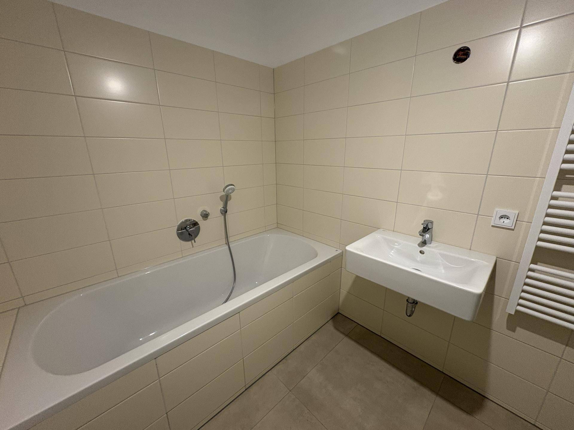 Helles Badezimmer mit Badewanne, modernem Waschbecken und beigefarbenen Wandfliesen, sehr gepflegt.