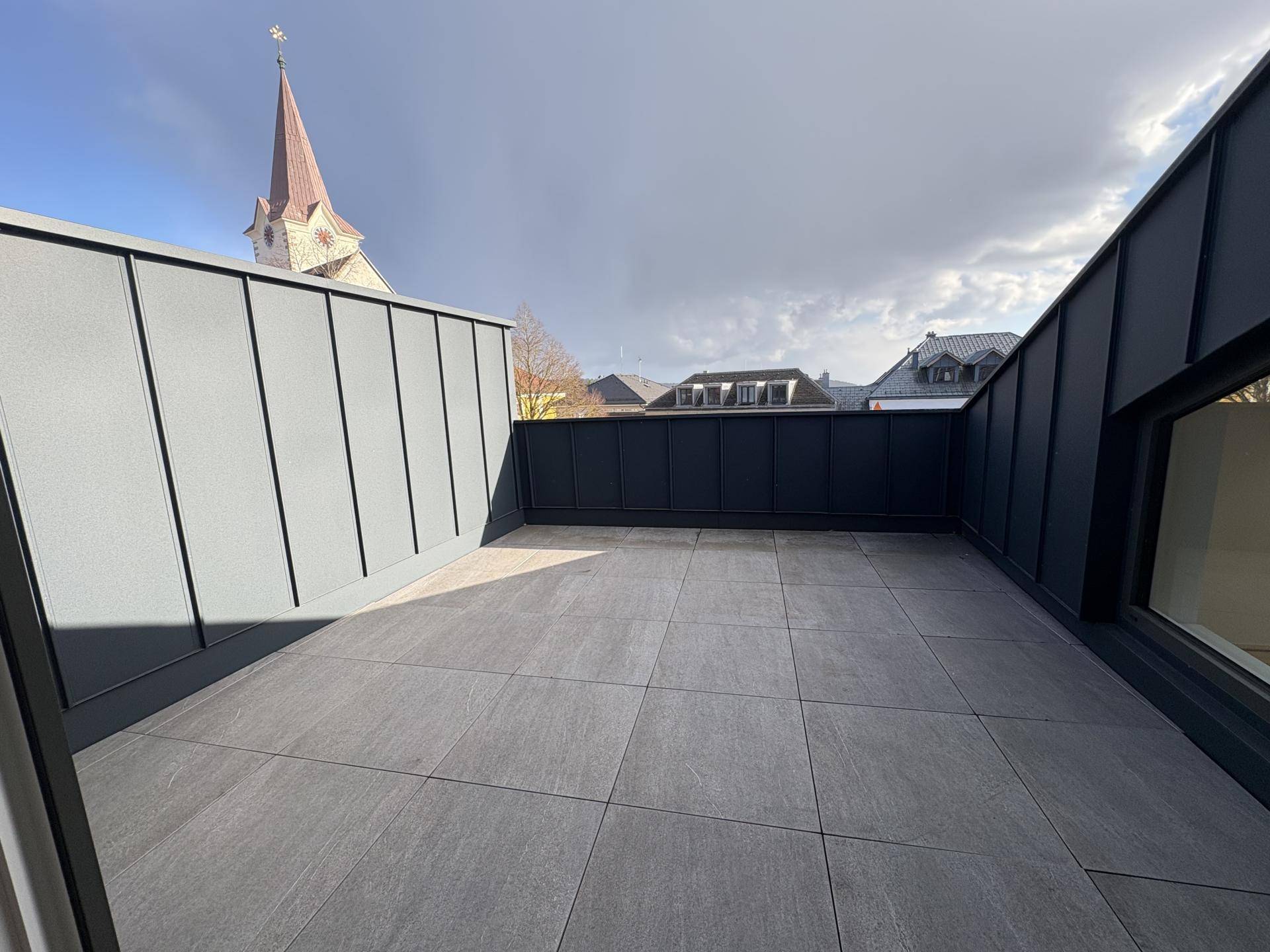 Geräumige Dachterrasse mit grauen Fliesen und einem malerischen Blick auf die Kirchturmspitze.