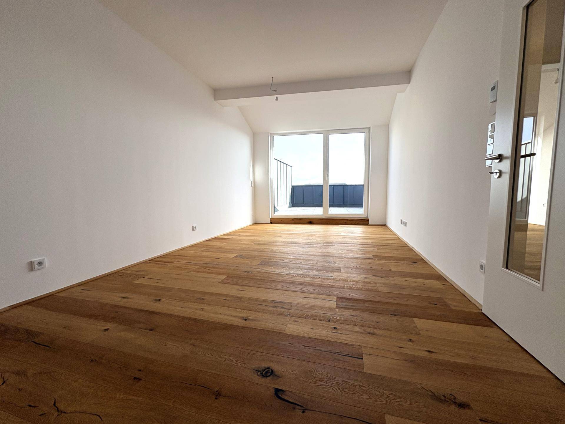 Lichtdurchfluteter Raum mit breiten Fensterfronten und Zugang zu einem Außenbereich, ausgestattet mit Holzboden.