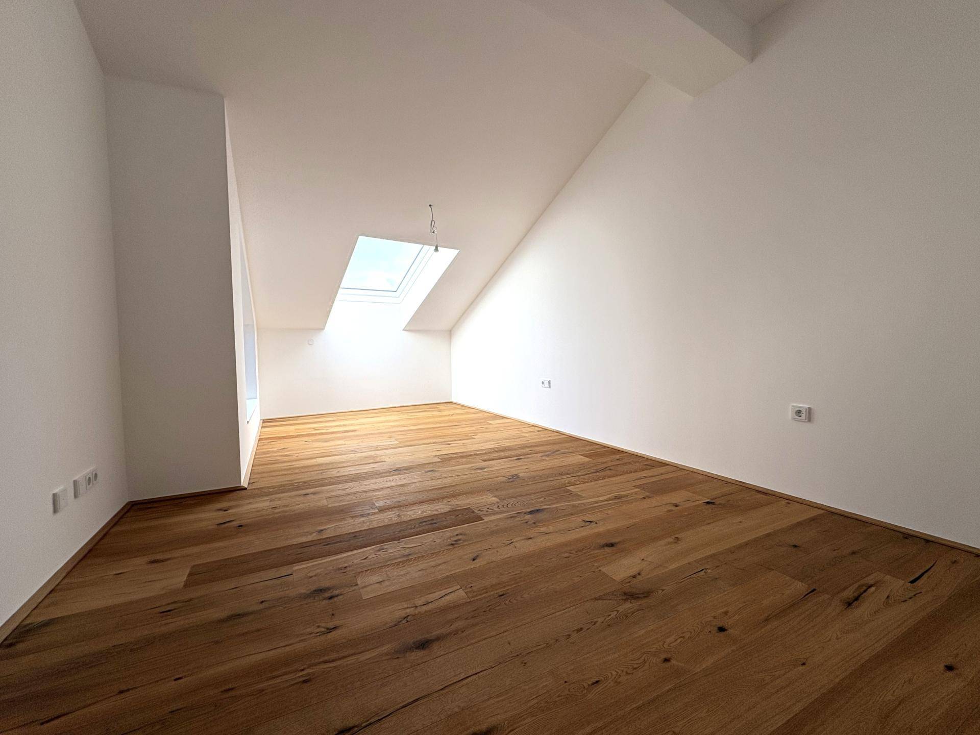 Helles Zimmer im Dachgeschoss mit Holzboden und einem großen Dachfenster, ideal als Schlafzimmer.