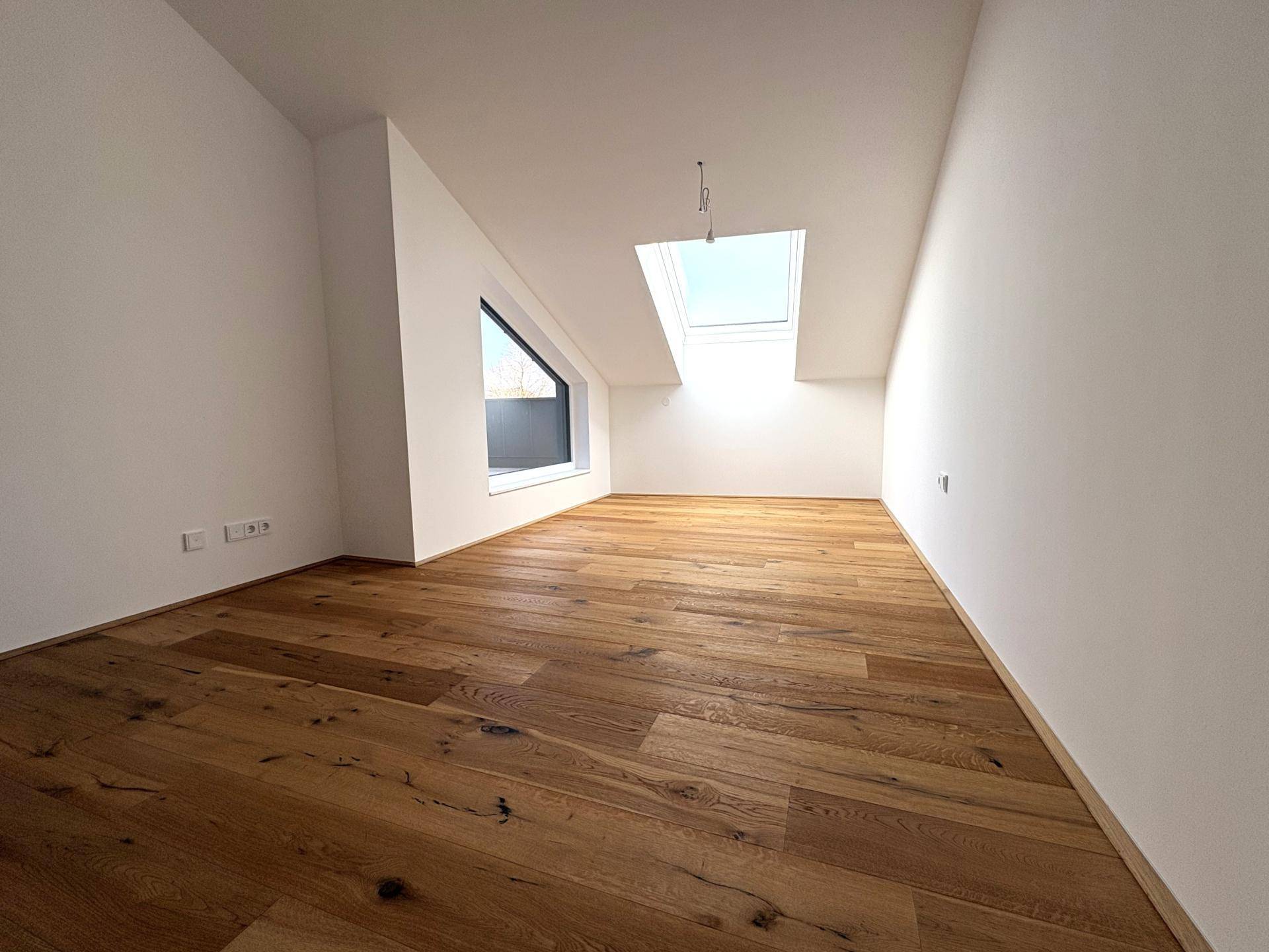 Gemütliches Schlafzimmer im Dachgeschoss mit Holzboden, Dachfenster und schräger Wand für viel Tageslicht.