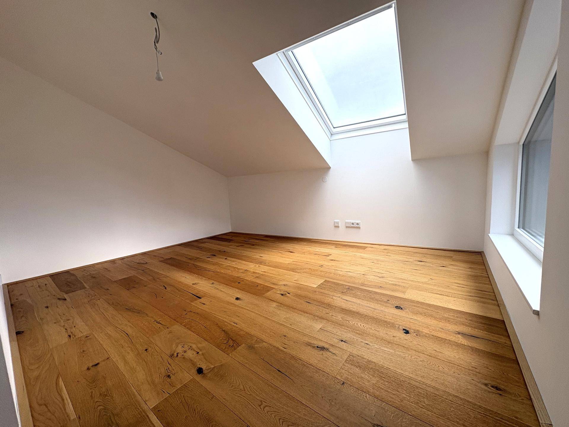 Helles Dachzimmer mit Holzboden und großem Dachfenster, bietet viel natürliches Licht.
