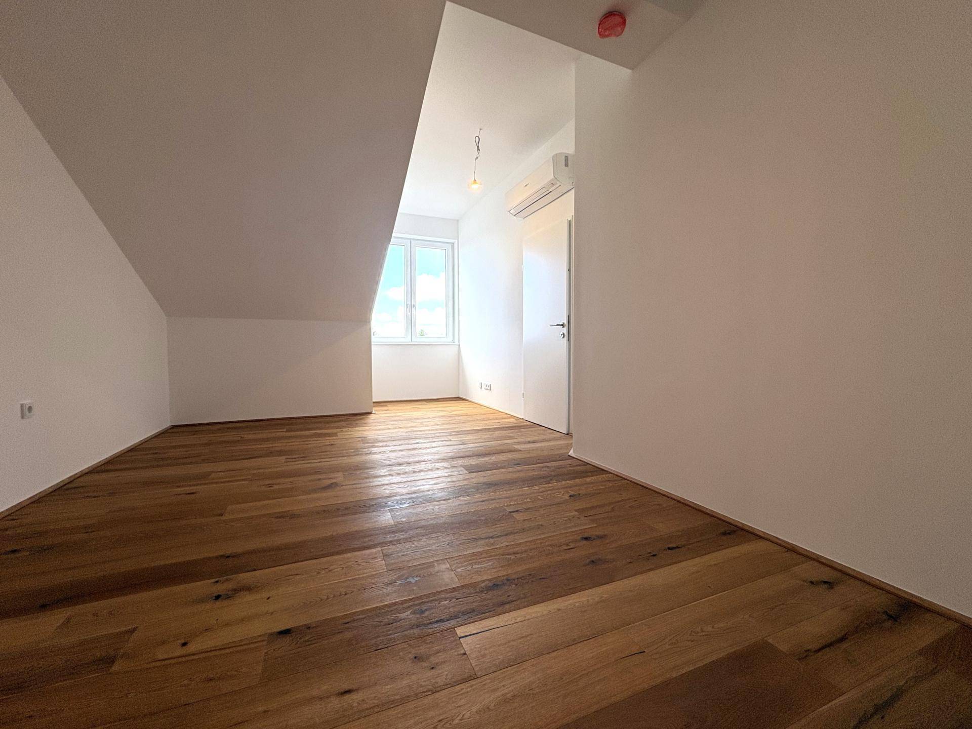 Gemütliches Schlafzimmer im Dachgeschoss mit Holzboden und schrägen Wänden, hell durch ein Fenster.
