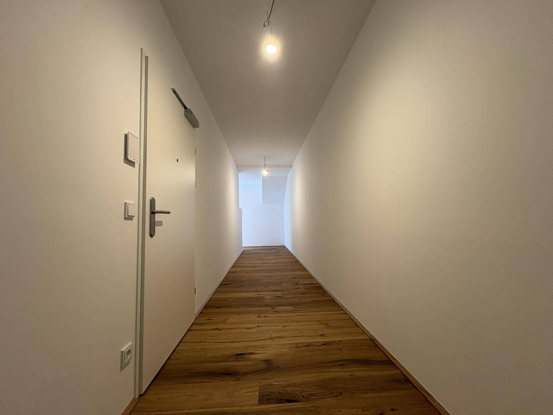 Langer, heller Flur mit Holzboden und weiß gestrichenen Wänden, führt in den Wohnbereich.