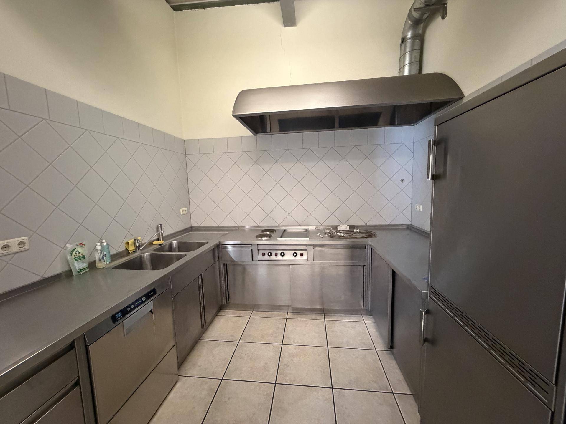 Industrielle Edelstahlküche mit Spülmaschine, Kochfeld und großer Dunstabzugshaube, ideal für Gastronomie.