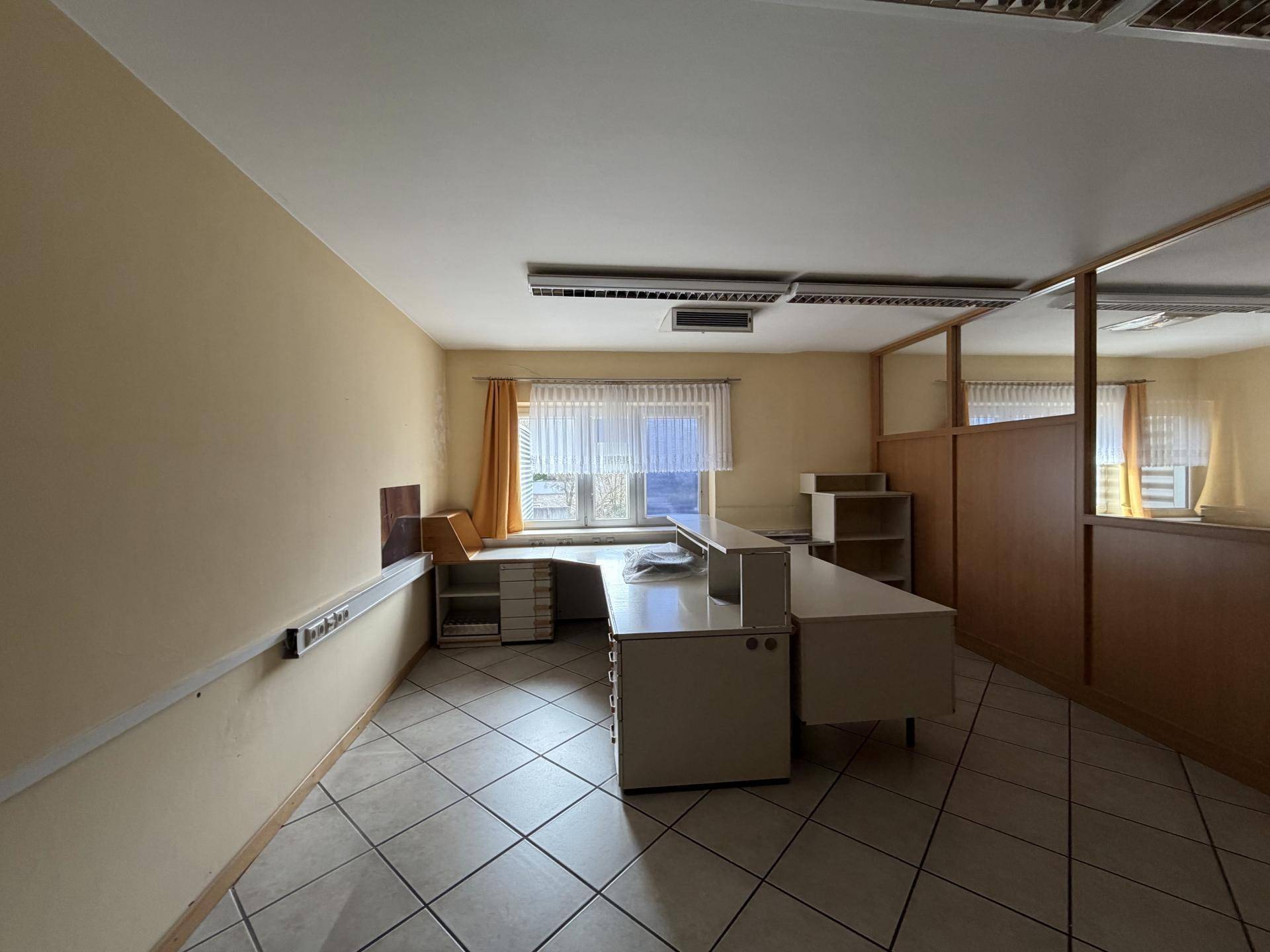 Leeres Büro mit Schreibtisch, Trennwänden und großen Fenstern, bietet viel natürliches Licht.