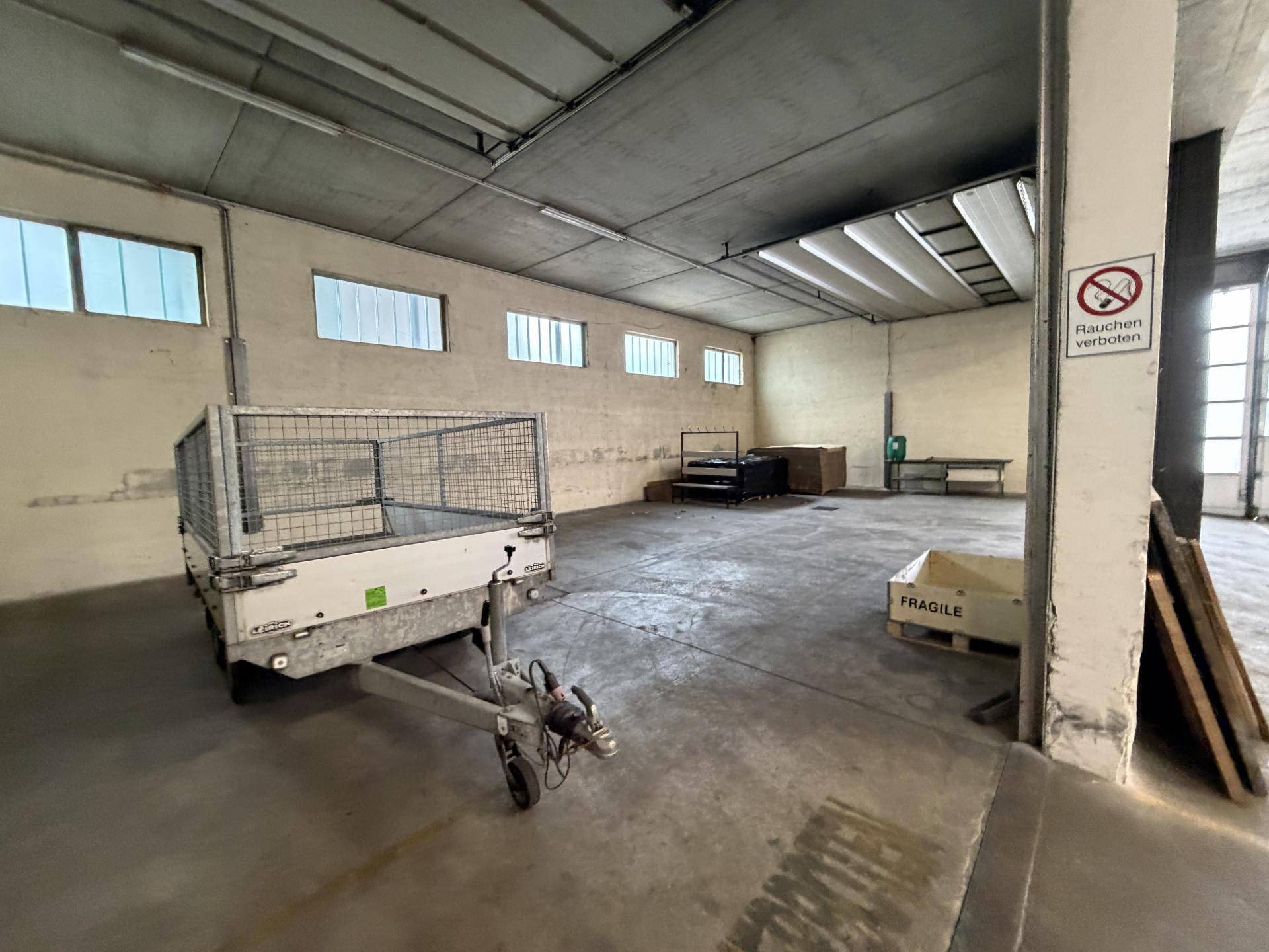 Geräumige Lagerhalle mit Betonboden, Anhänger und hohen Decken, bietet viel Platz für Lagerung.
