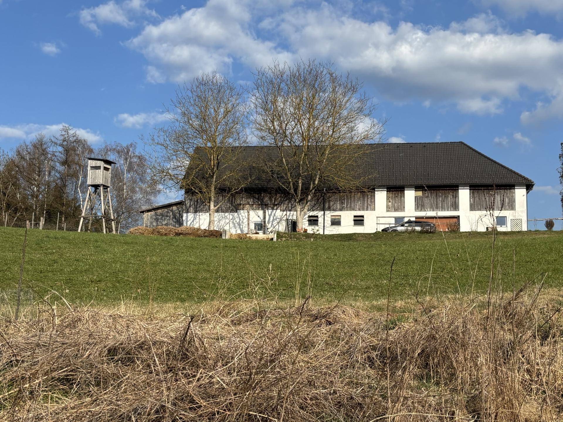 Weißes Gebäude im ländlichen Stil mit dunklem Dach und einem Hochsitz in der weiten Landschaft.