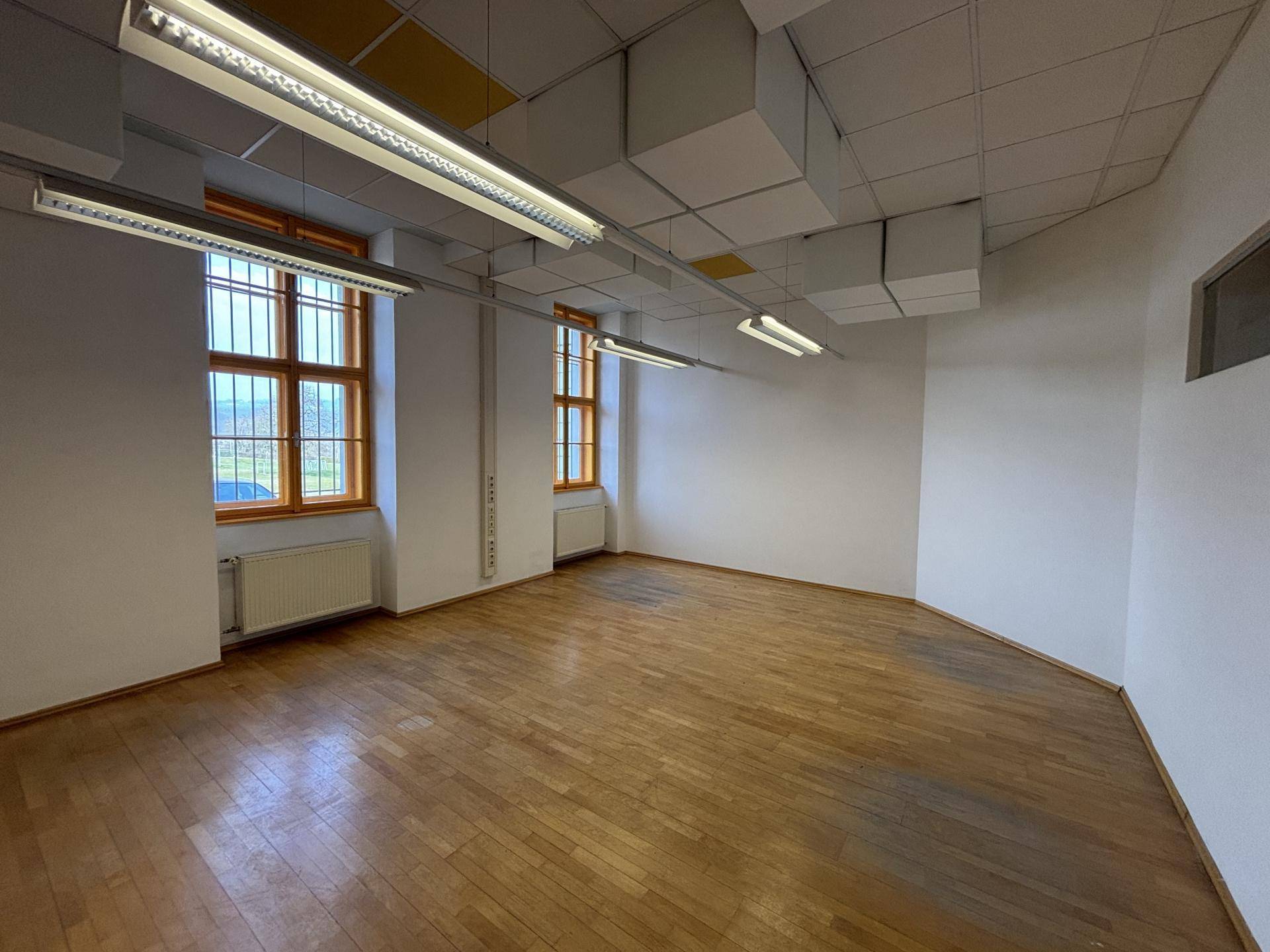 Geräumiger Büroraum mit Holzboden, großen Fenstern und abgehängter Decke mit Beleuchtung, bereit zur Nutzung.