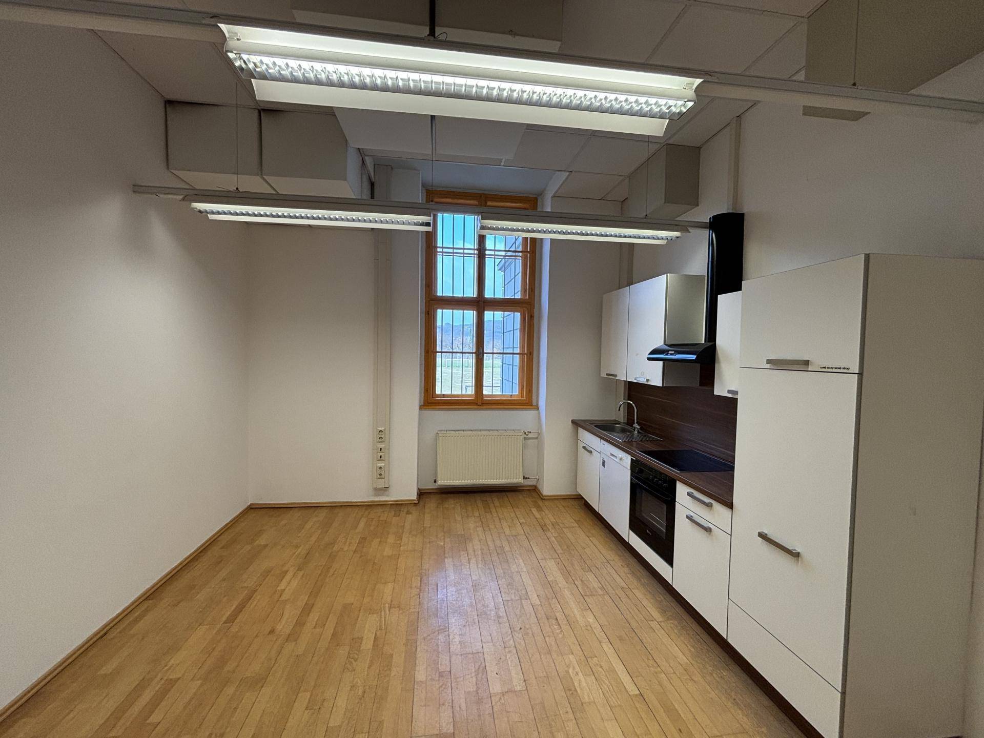 Kleine, funktionale Küchenzeile in einem Raum mit Holzboden und Fenster, ausgestattet mit Herd und Kühlschrank.
