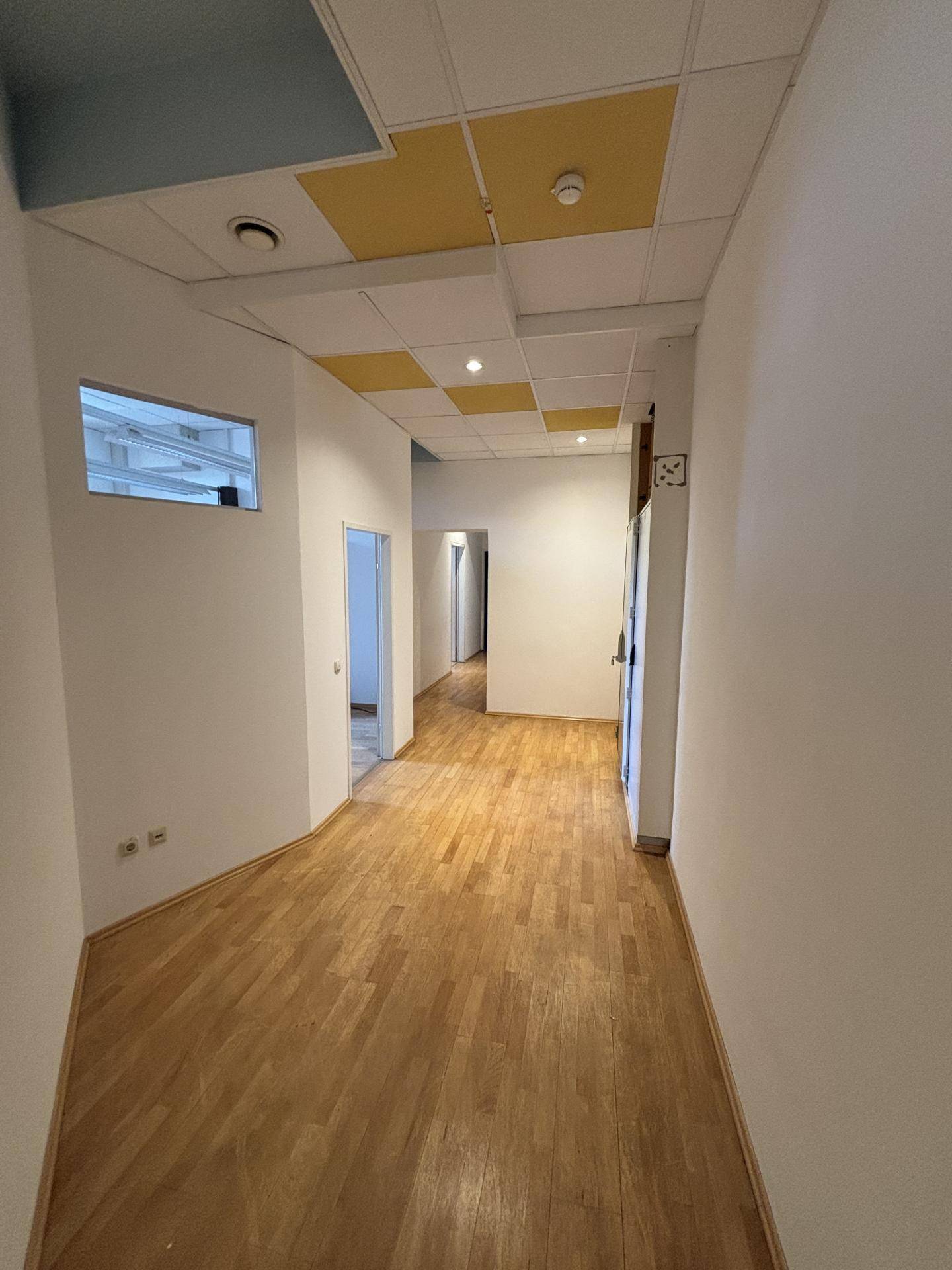 Langer Flur mit Holzboden und abgehängter Decke, der zu verschiedenen Büroräumen führt.