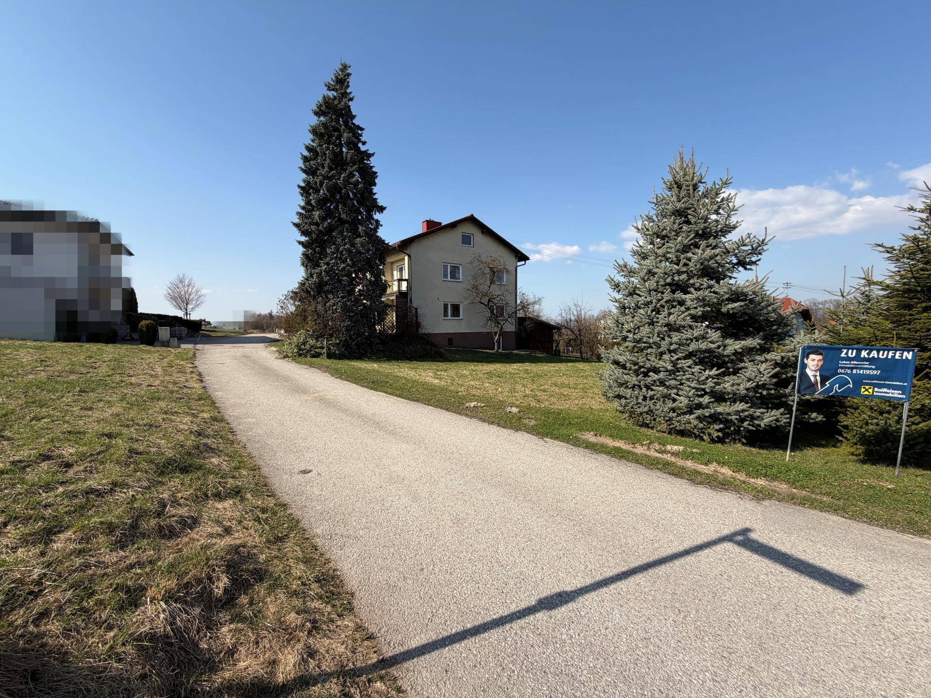 Zufahrtsweg zum Grundstück mit einem Wohnhaus und einem Verkaufsschild.