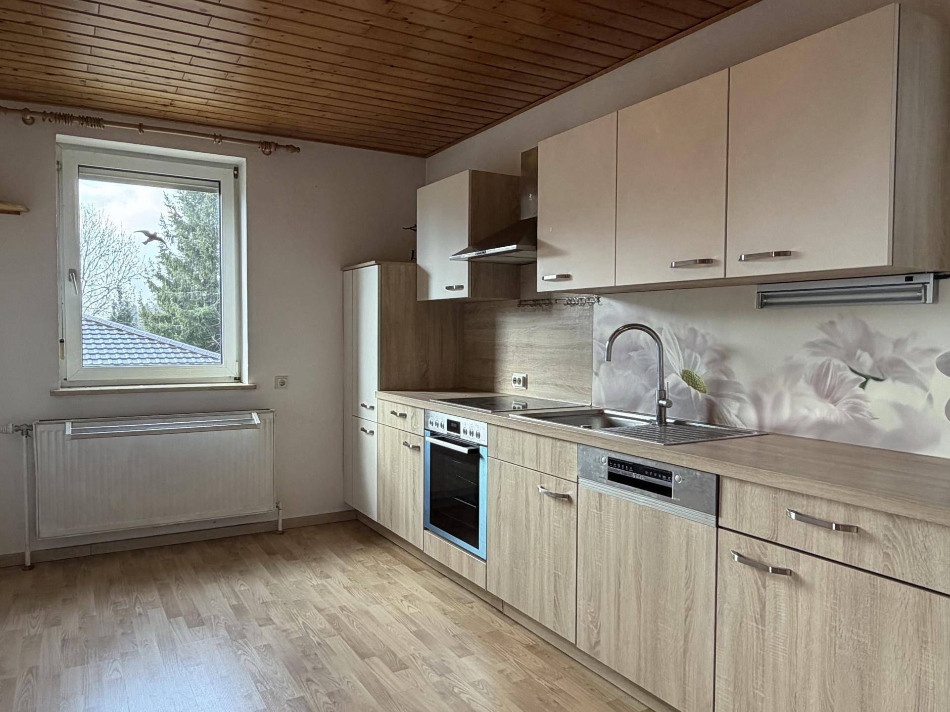 Geräumige Küche mit Holzdecke, Einbaumöbeln und Blick ins Grüne durch das Fenster.