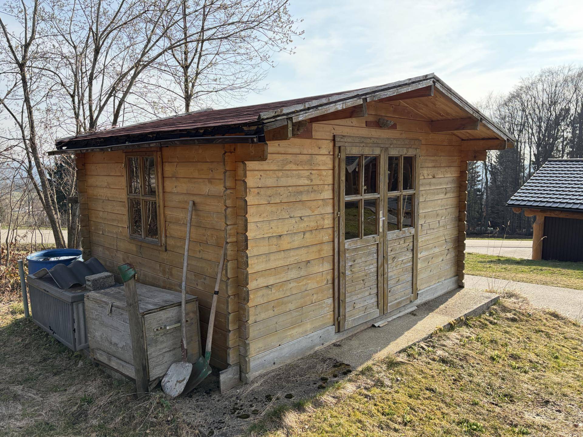 Rustikaler Holzschuppen mit Doppeltür und Fenster in ländlicher Umgebung.