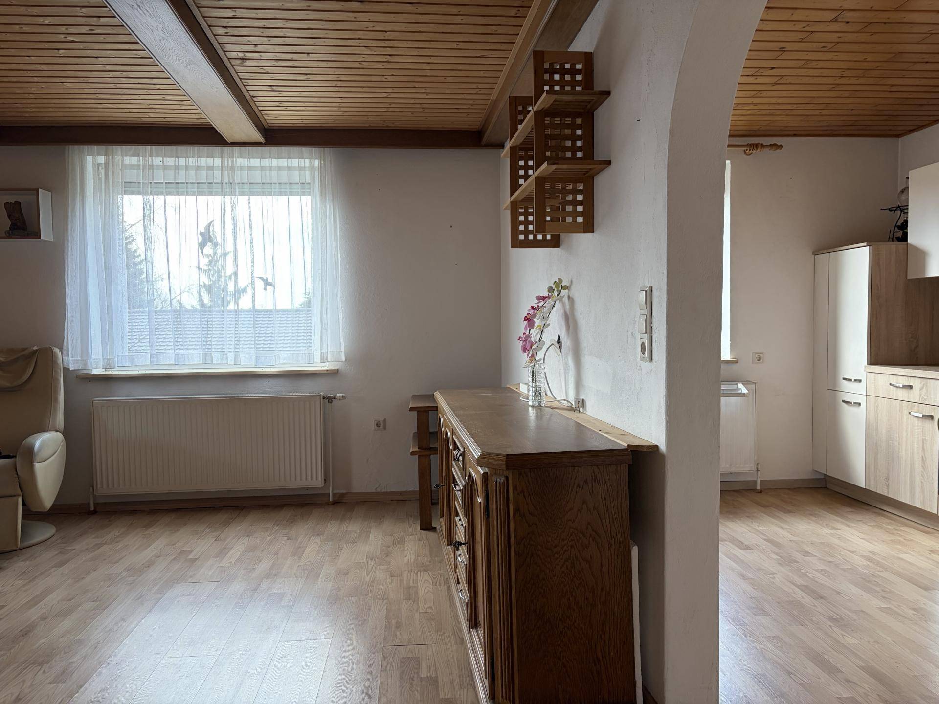 Gemütlicher Wohnbereich mit Holzdecke, Laminatboden und Fenster mit Vorhängen.