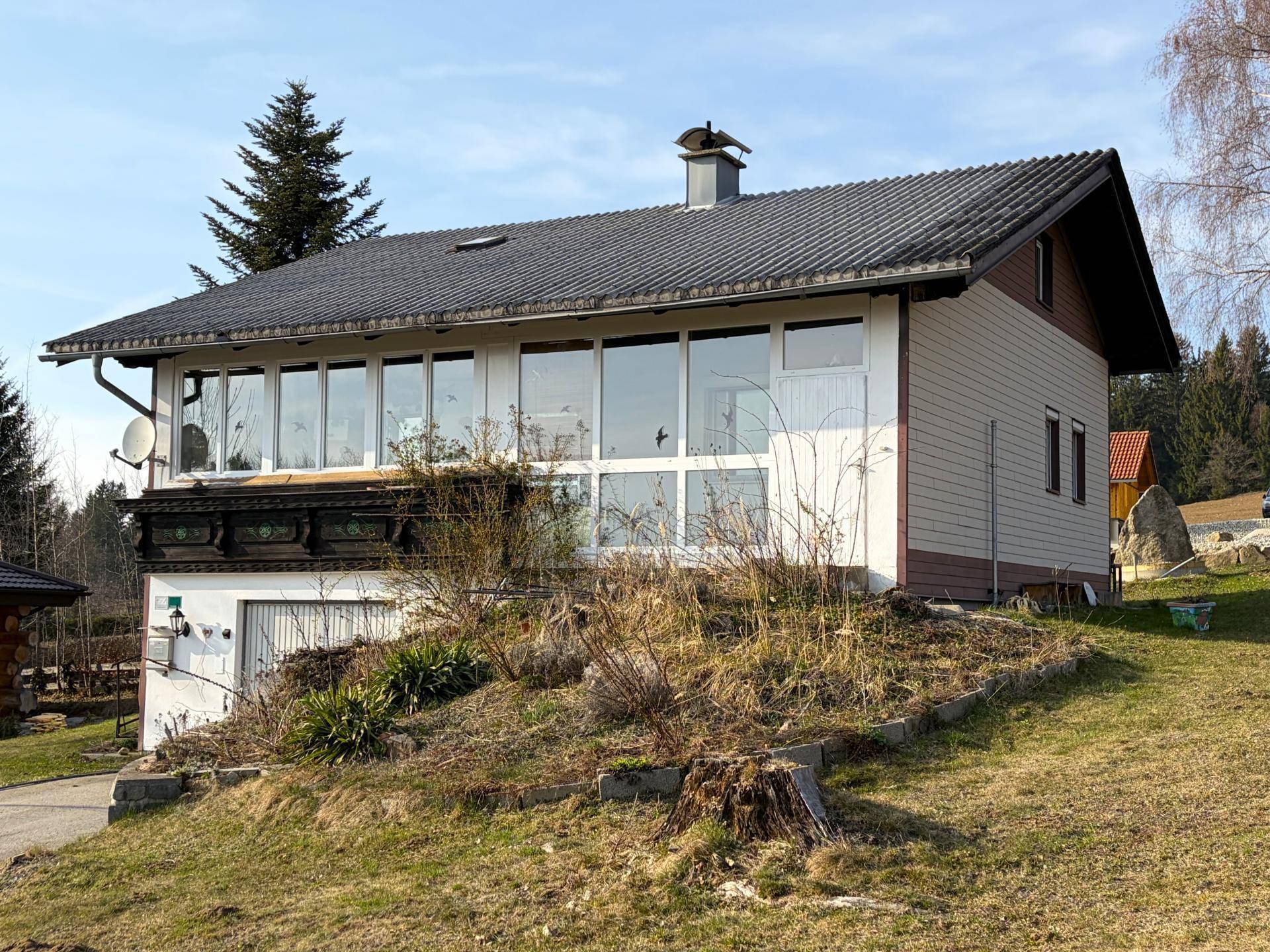 Ländliches Einfamilienhaus mit großflächigen Fenstern, Satteldach und kleinem Balkon in grüner Umgebung.