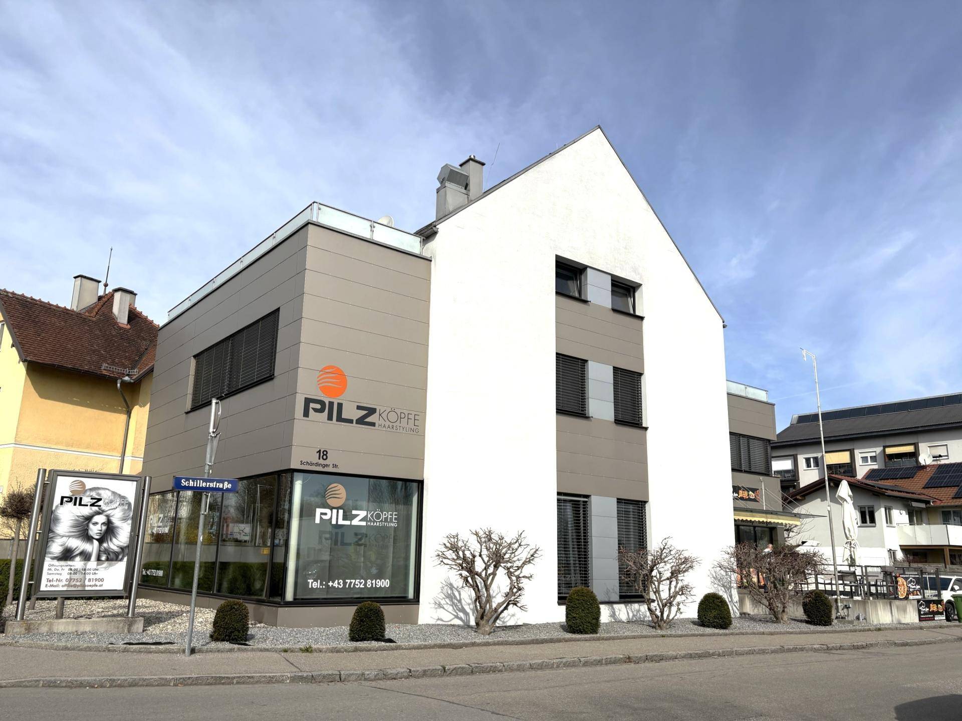 Ansicht des modernen Gebäudes mit grauer und weißer Fassade sowie großen Fenstern.