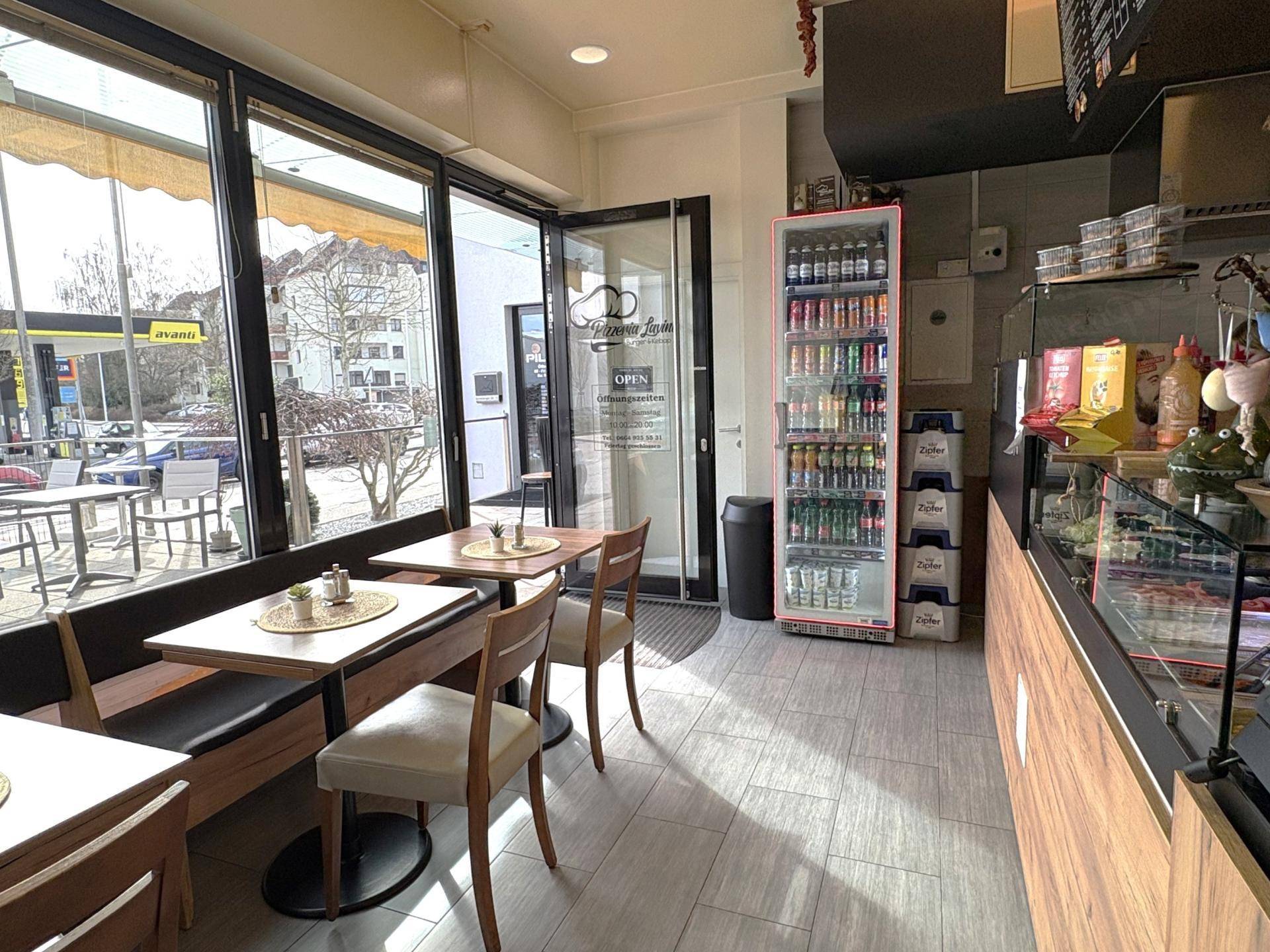 Innenansicht eines Cafés mit Sitzgelegenheiten, großen Fenstern und einer Theke.