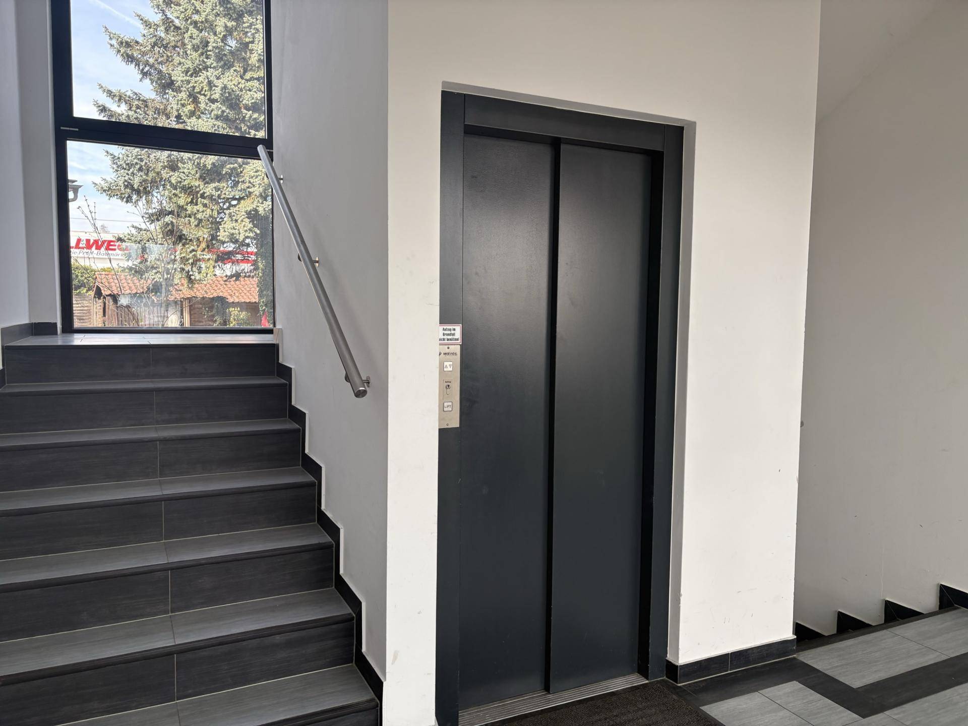 Treppenhaus mit Fliesenstufen und einem modernen Aufzug für bequemen Zugang.