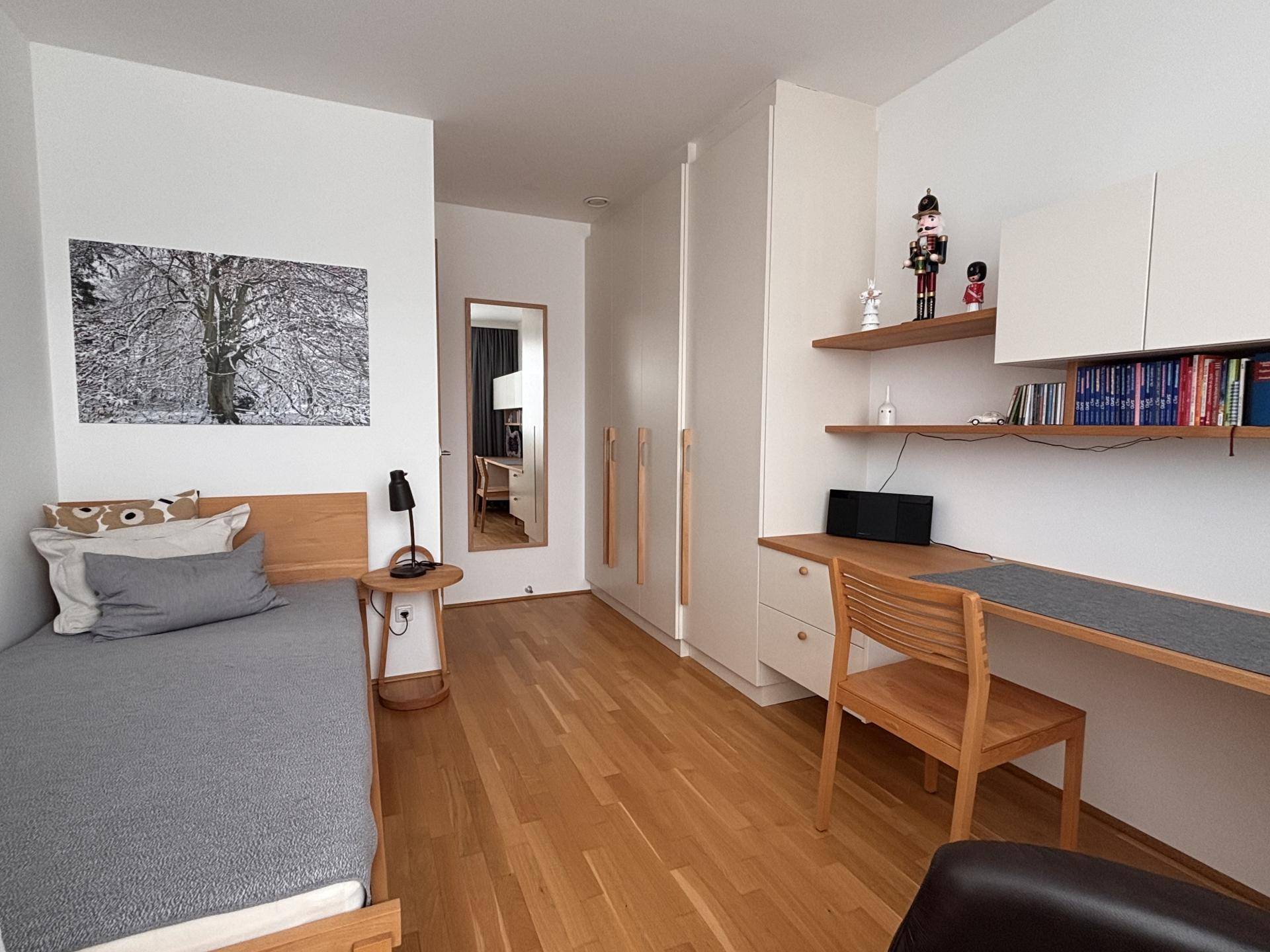 Schlafzimmer mit Einzelbett, Holzfußboden und integriertem Schreibtischbereich.