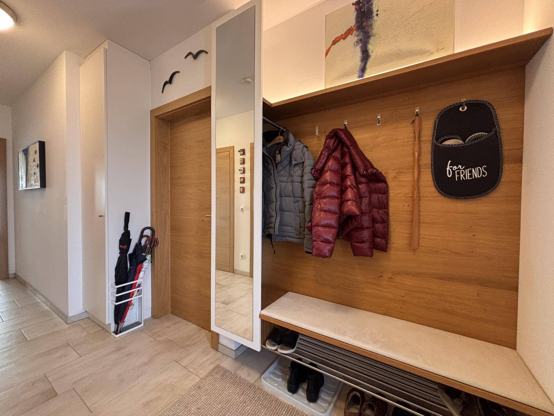 Eingangsbereich mit Holzvertäfelung, Garderobe, Sitzbank und großem Spiegel.