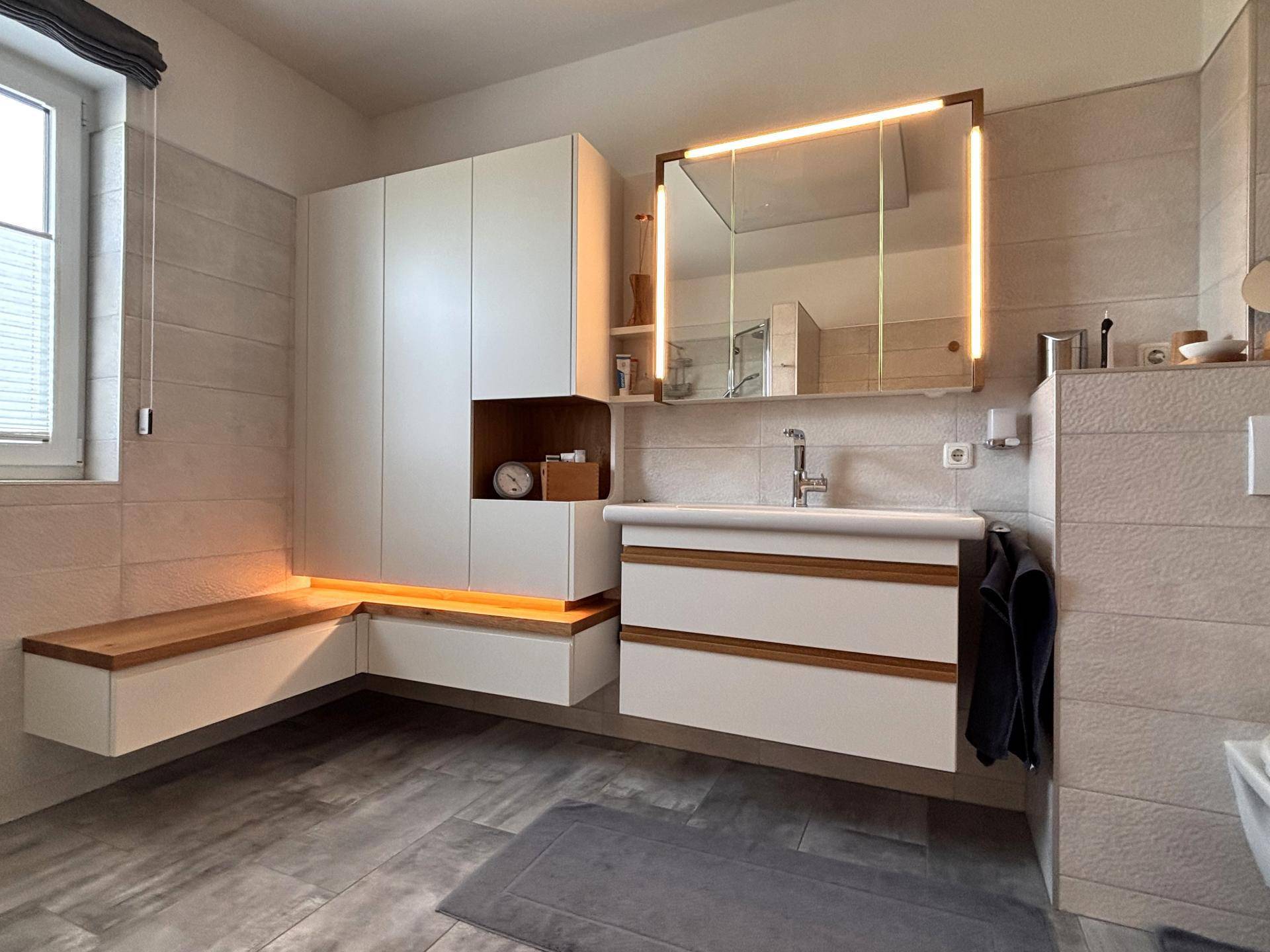 Modernes Badezimmer mit beleuchtetem Spiegelschrank, Einzelwaschbecken und schwebendem Waschtisch.